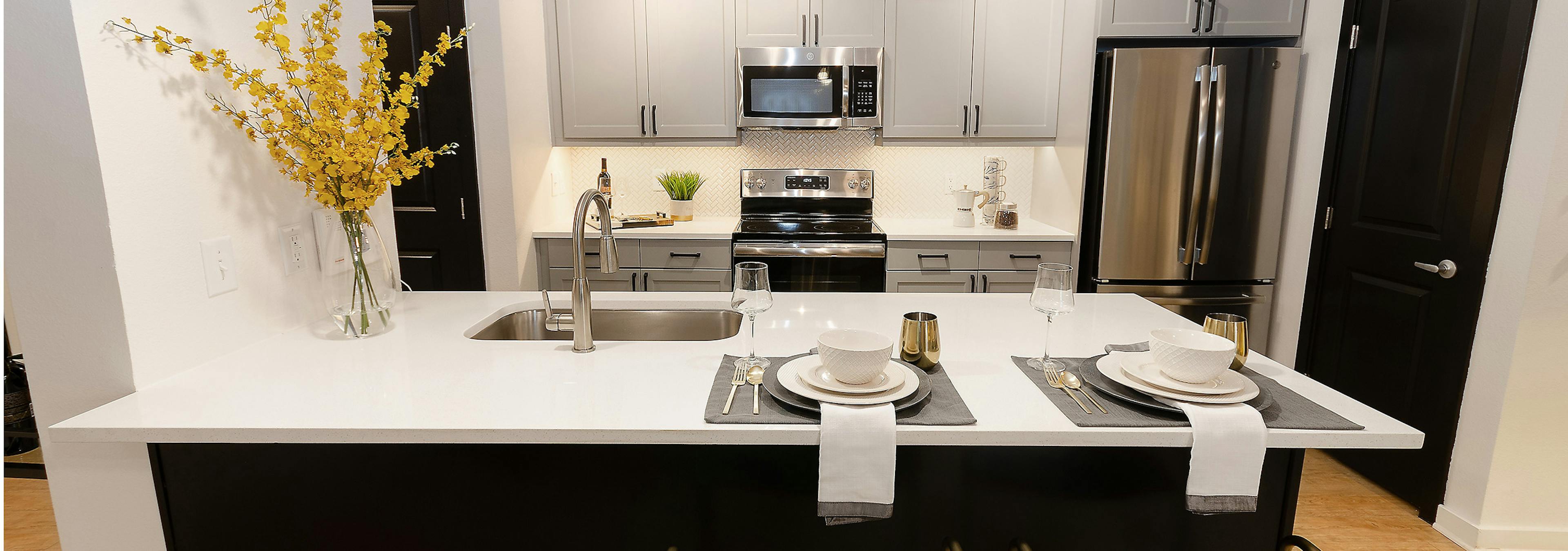 Island kitchen at AMLI Quadrangle with sleek white counters with grey cabinets and stainless steel appliances in background