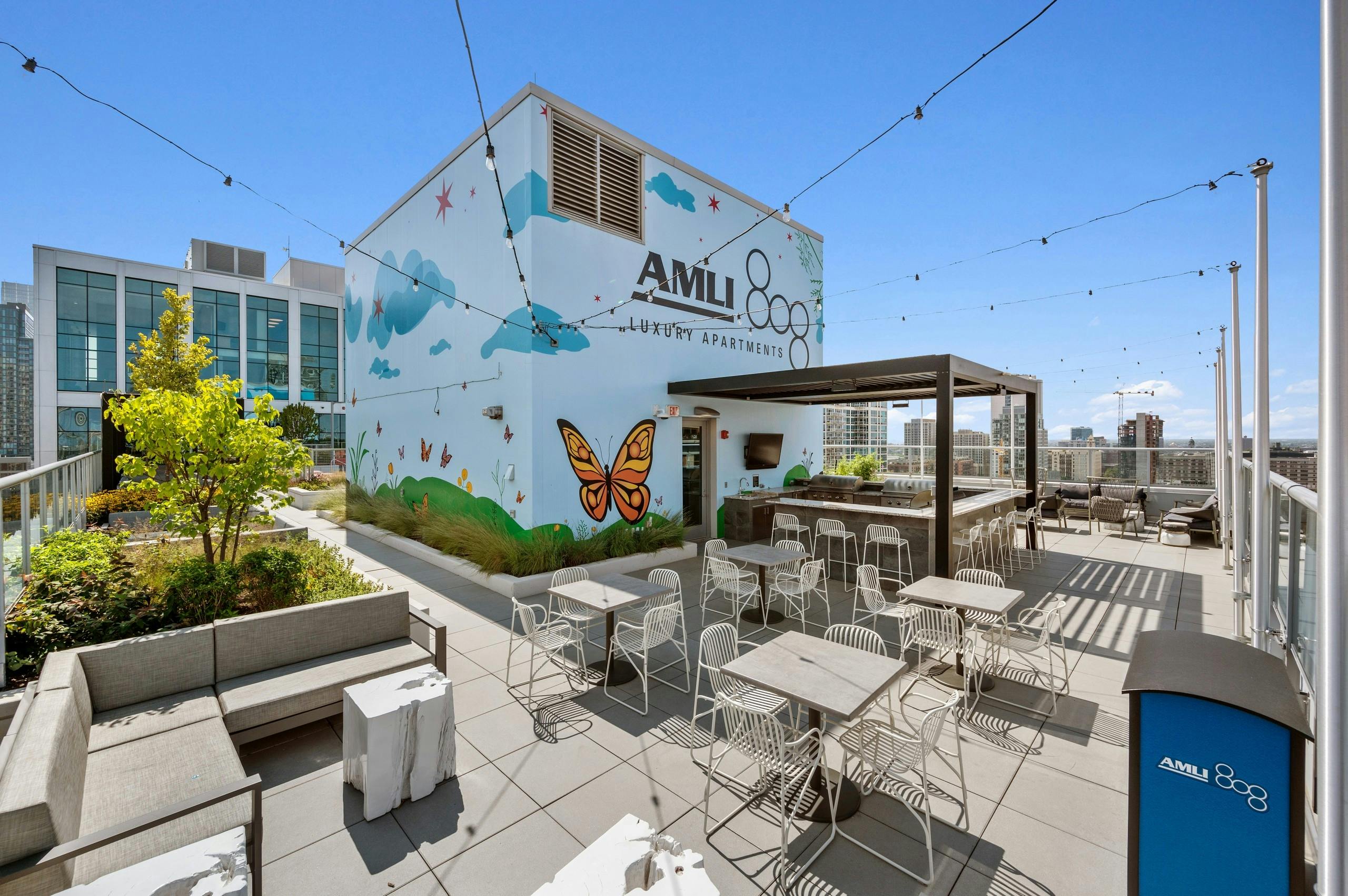 Rooftop with large colorful mural as backdrop to tables and chairs surrounding grill station at the AMLI 808