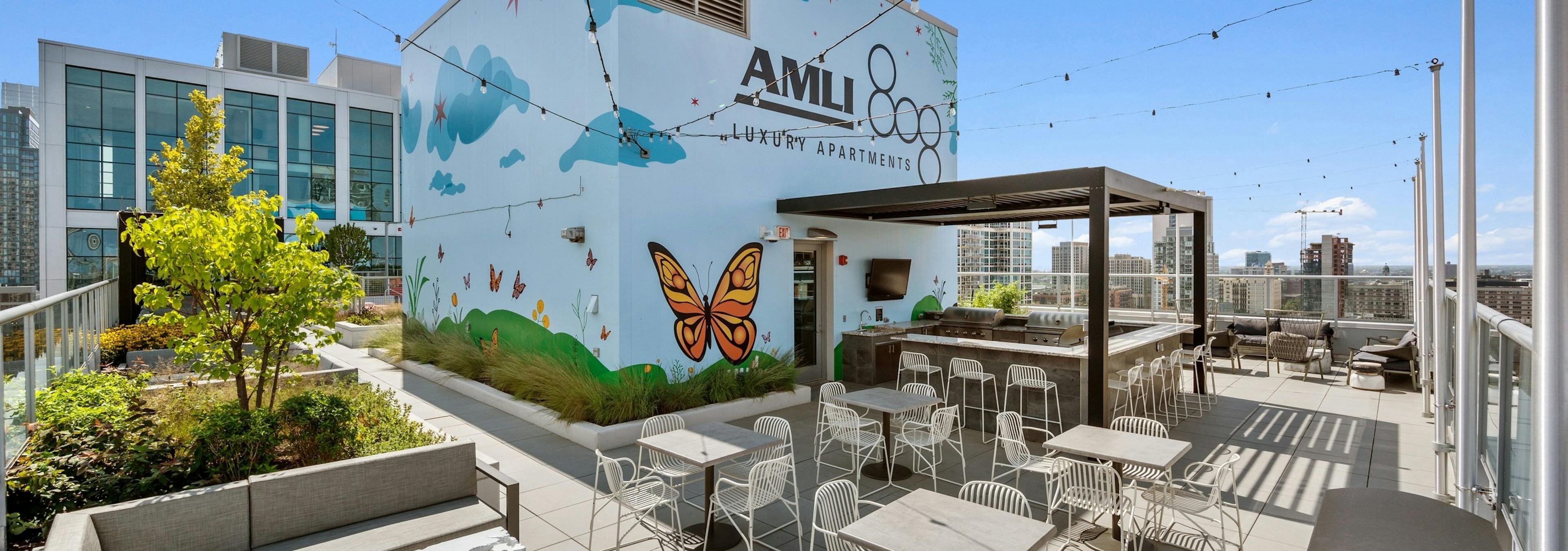 Rooftop with large colorful mural as backdrop to tables and chairs surrounding grill station at the AMLI 808
