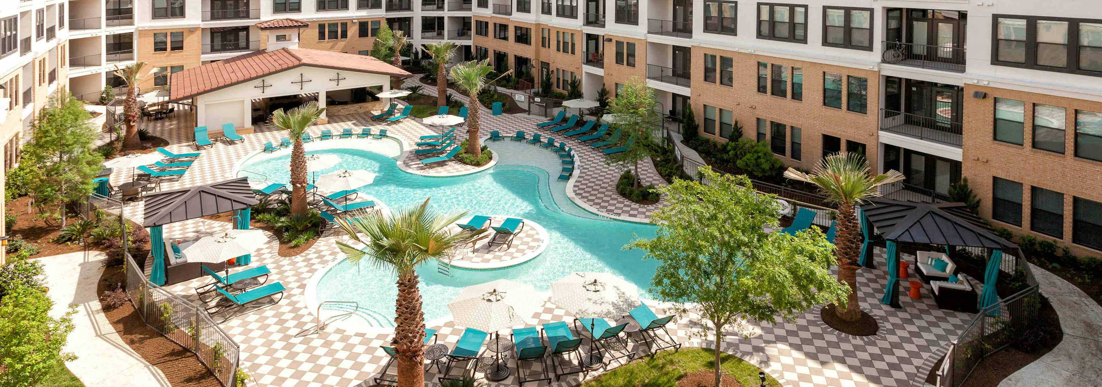 Daytime aerial view of AMLI Campion Trail landscaped swimming pool area with lounge seating, cabanas and palm trees