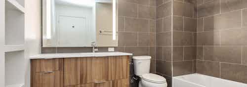 AMLI on 2nd bathroom with shower tub with large brown wall tiles and toilet with single vanity sink and built in white shelf