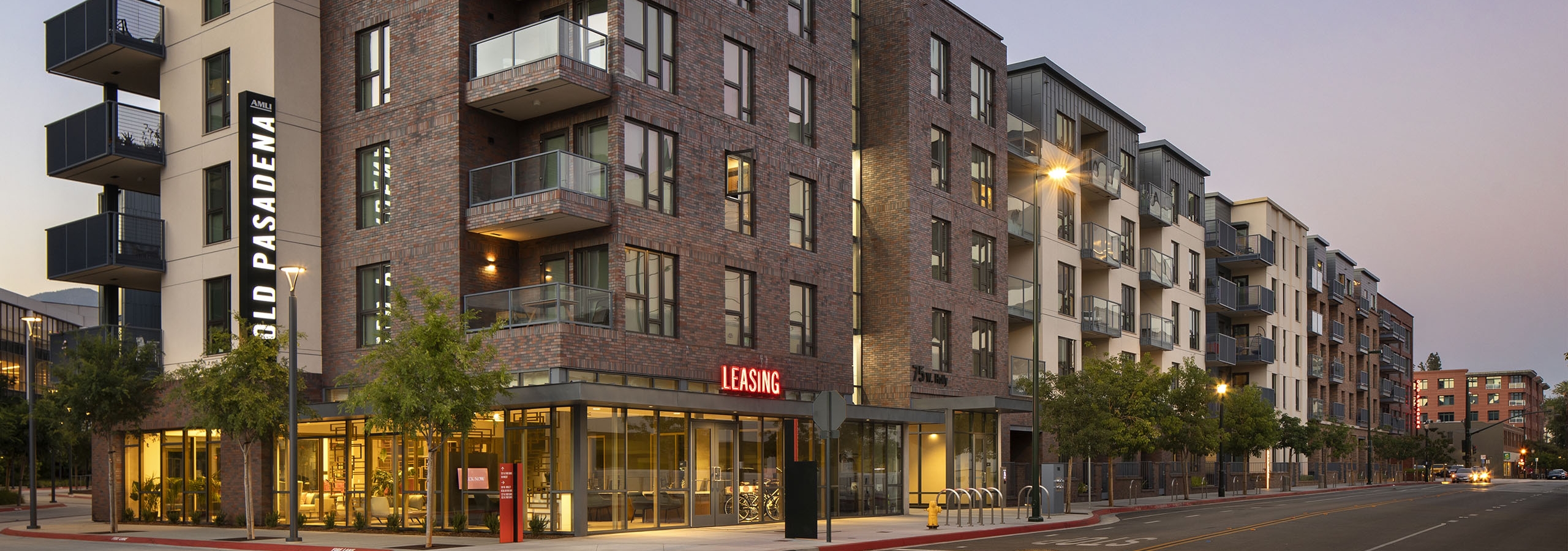 Panoramic view of AMLI Old Pasadena apartment building at dusk with first floor leasing office and monument signs lit up