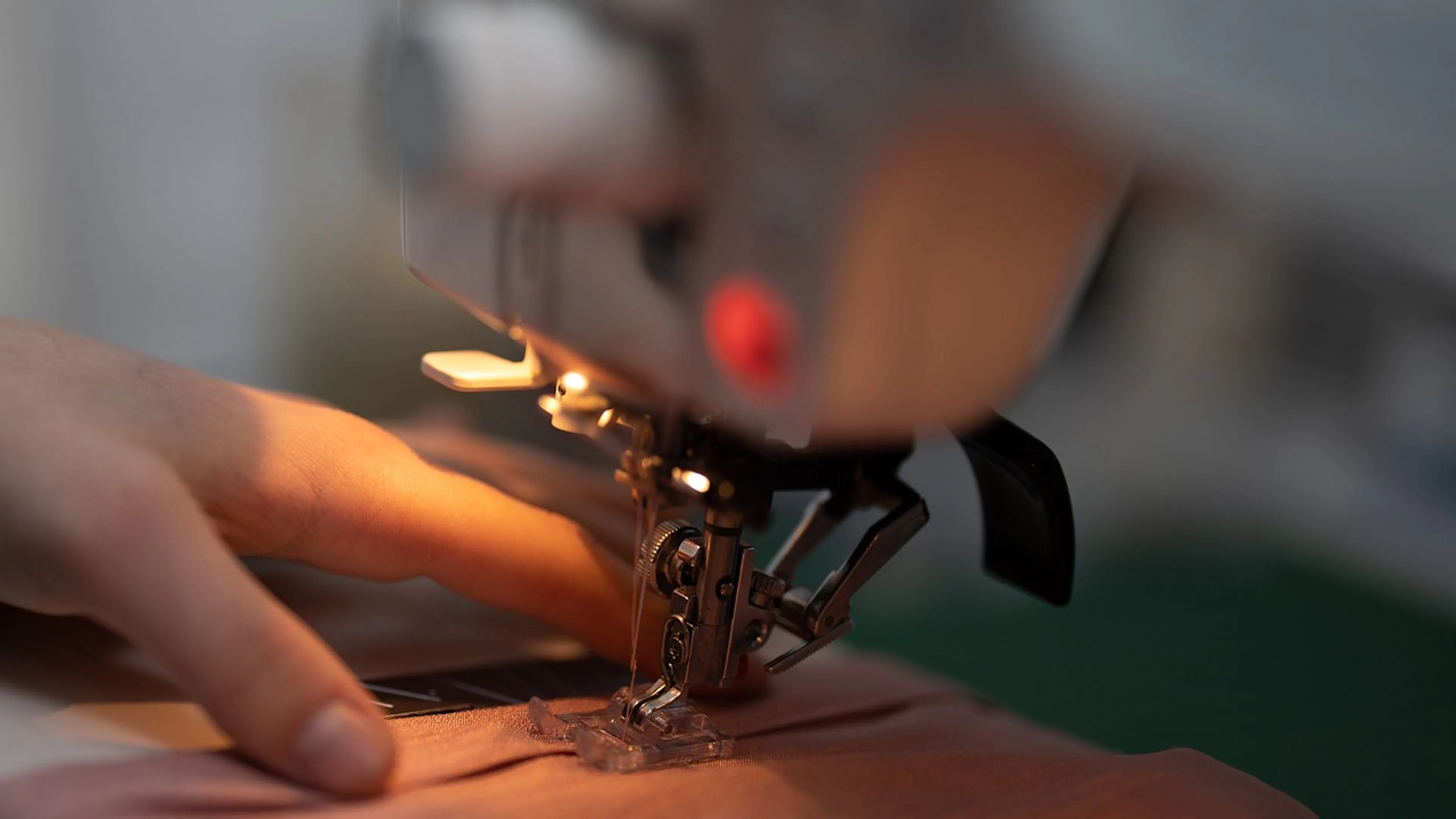 An extreme close up of a sewing machine foot and a person's hand sewing some pink fabric