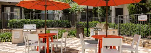Barbecue area at AMLI on Riverside with orange tables and white chairs under umbrellas with shrubs and stainless steel grills