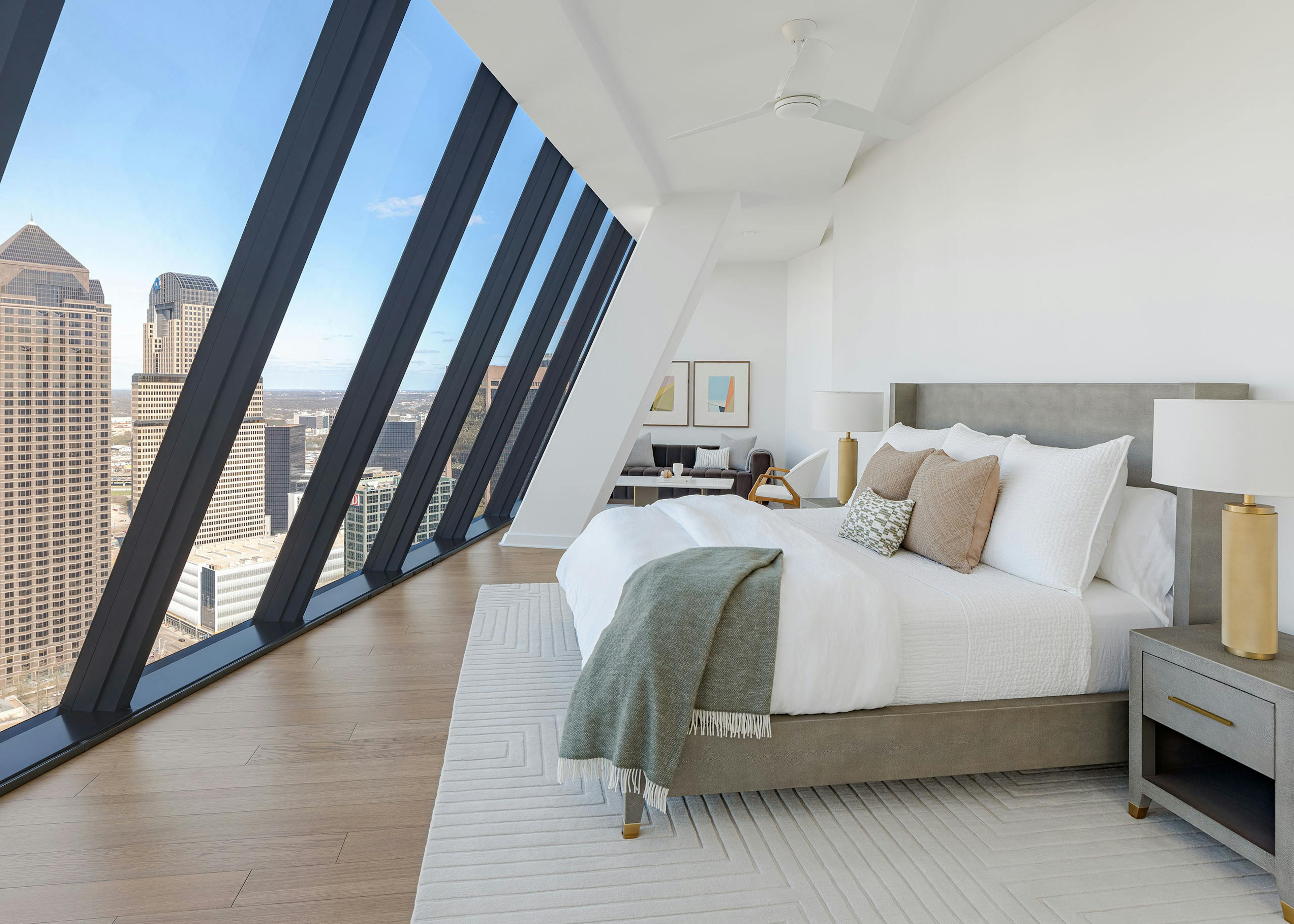 Sloped floor to ceiling windows in AMLI Fountain Place apartment with white walls and king bed with white rug on wood floor
