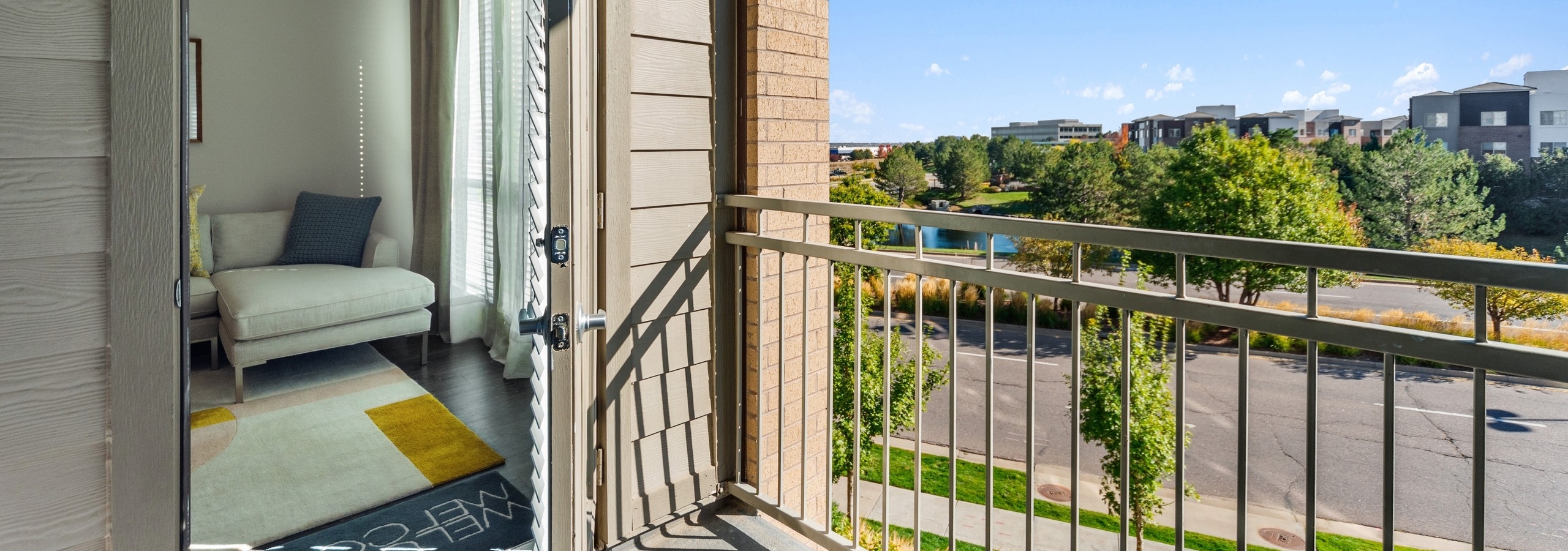 Balcony with beige railing at AMLI Dry Creek with view into living room and view of other buildings and tree lined street