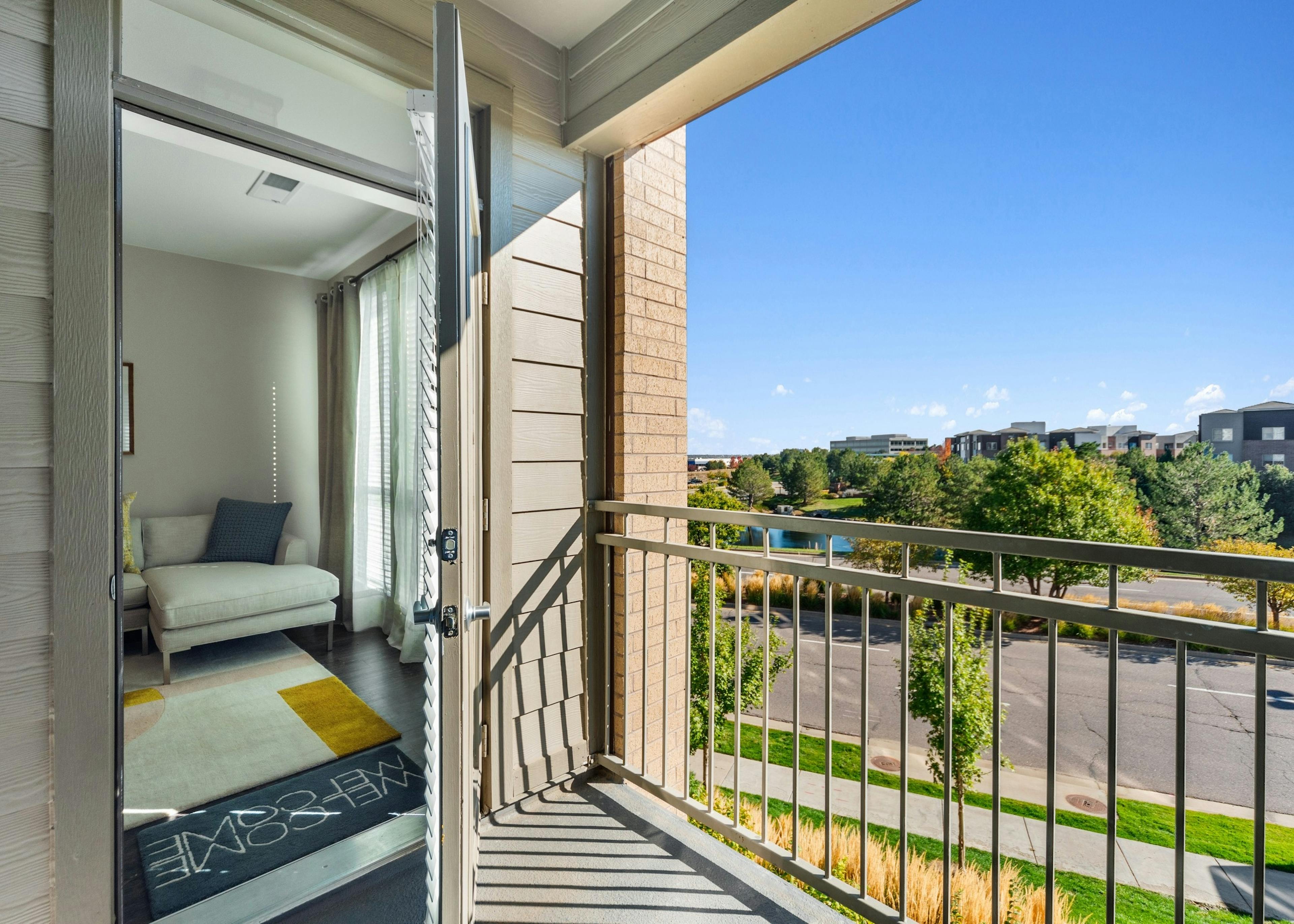 Balcony with beige railing at AMLI Dry Creek with view into living room and view of other buildings and tree lined street