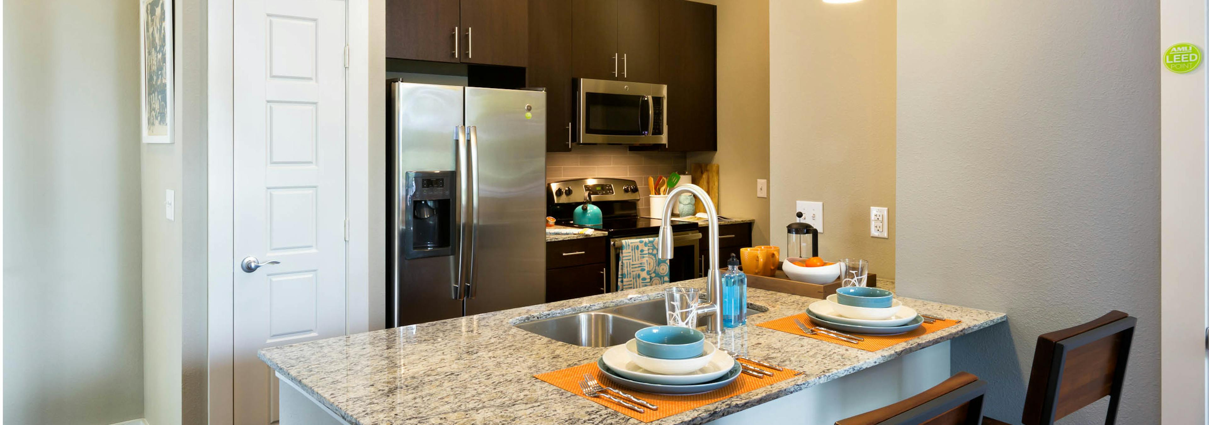 AMLI at Mueller kitchen with stools at a granite counter with dark wood cabinets and stainless steel appliances in background