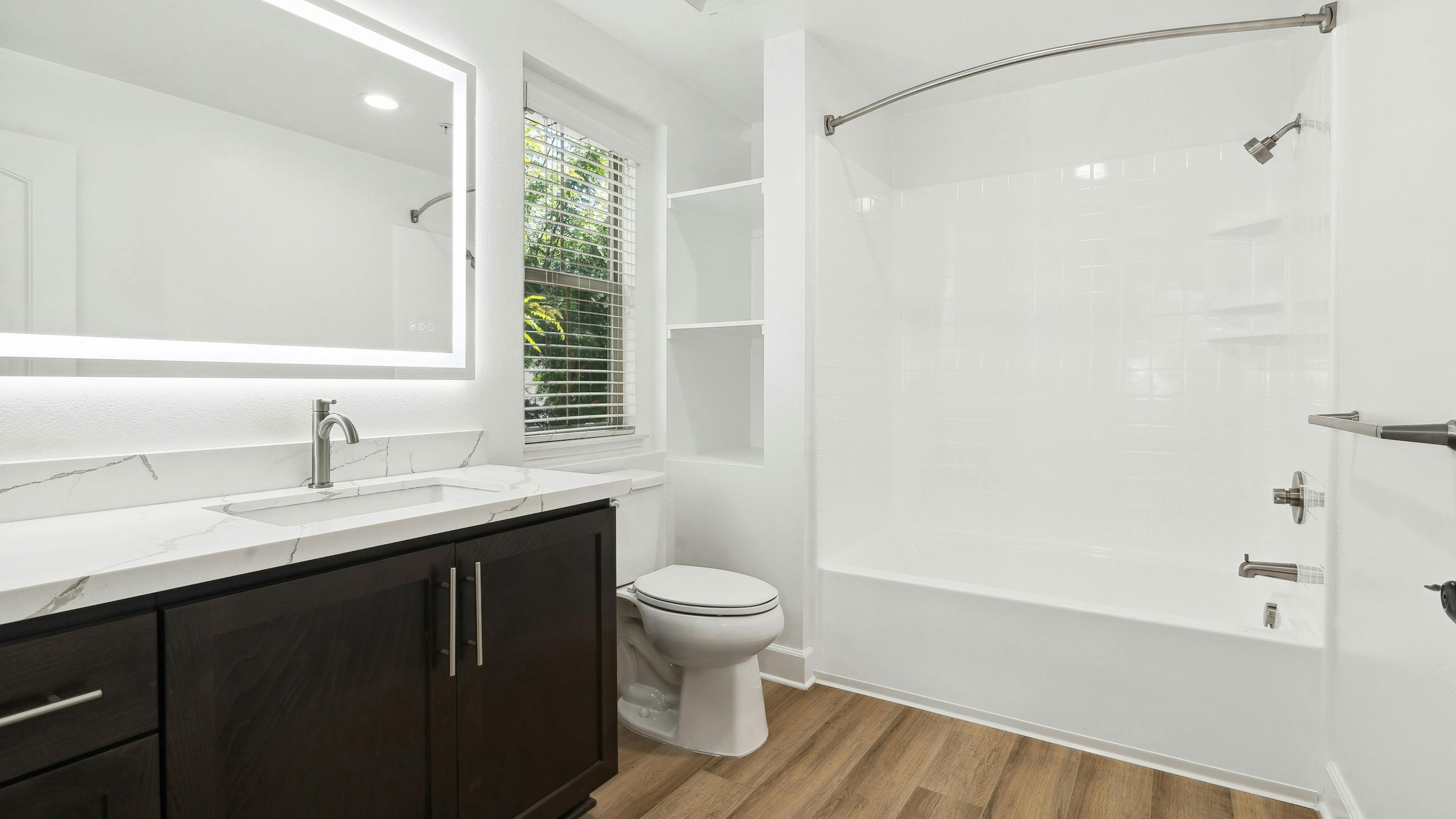 Bathrooms at AMLI Spanish Hills apartments with a brown vanity with white quartz countertop and white tub with tile surround 