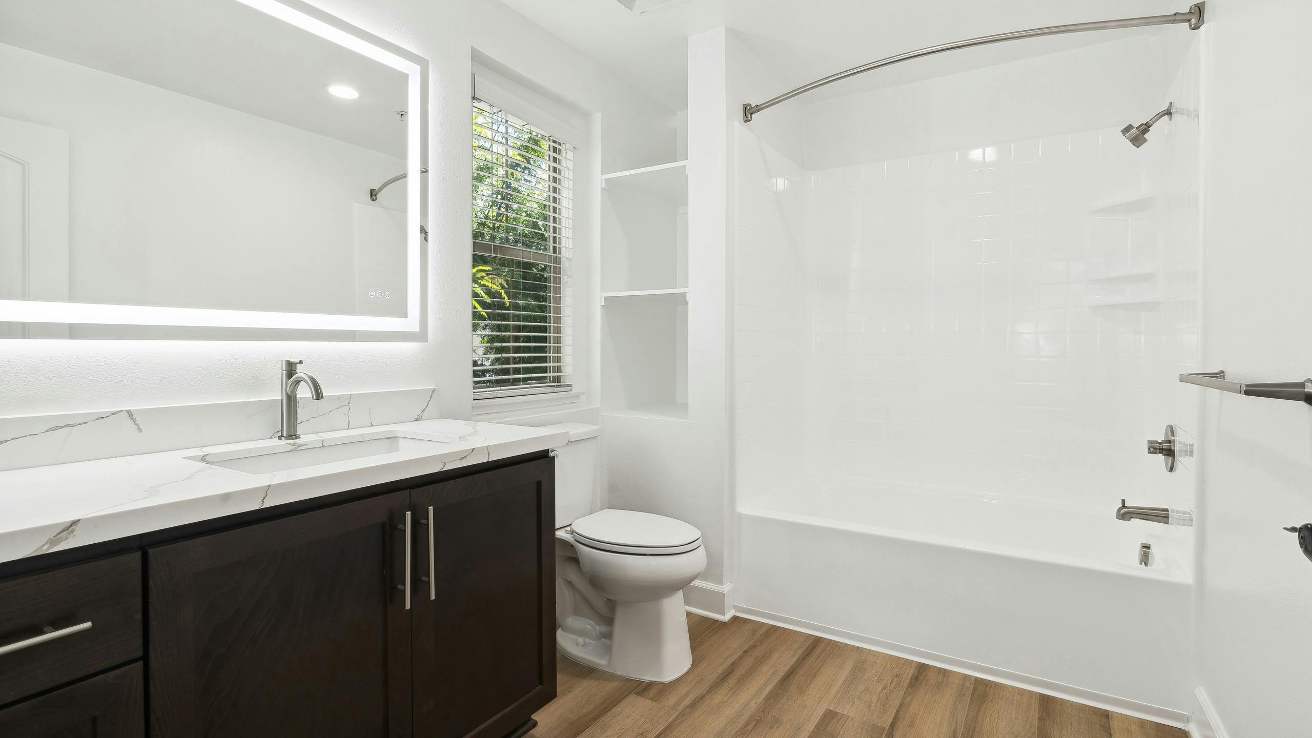 Bathrooms at AMLI Spanish Hills apartments with a brown vanity with white quartz countertop and white tub with tile surround