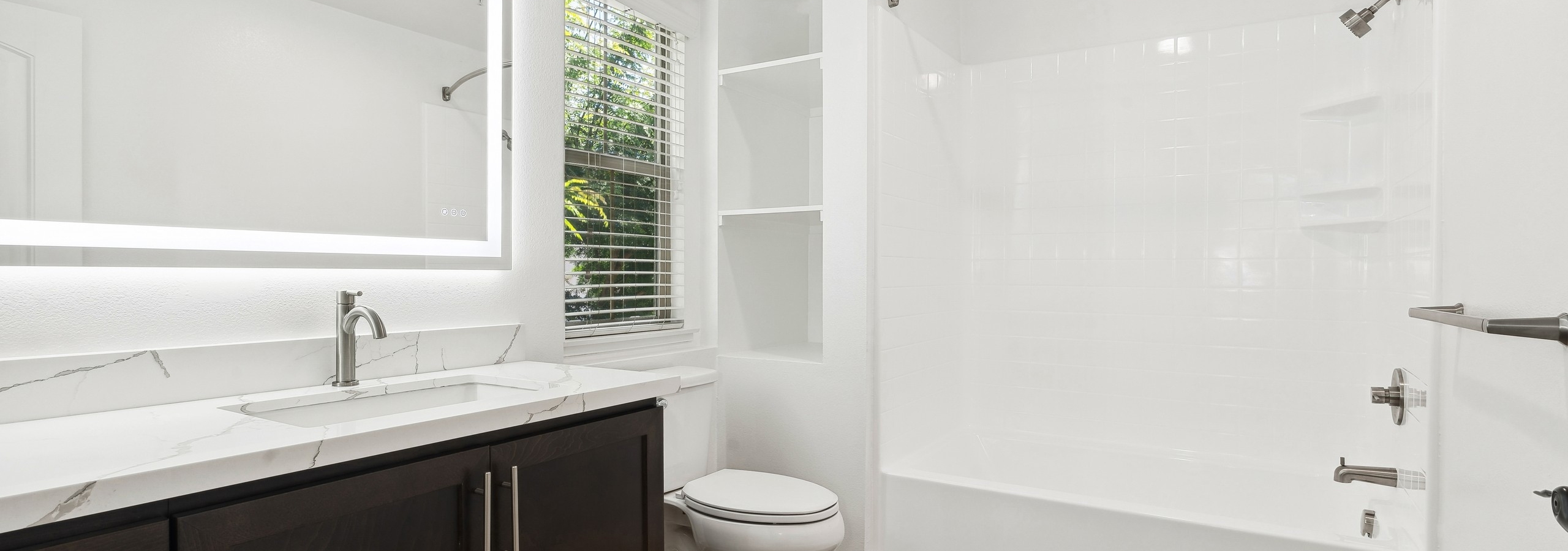 Bathrooms at AMLI Spanish Hills apartments with a brown vanity with white quartz countertop and white tub with tile surround