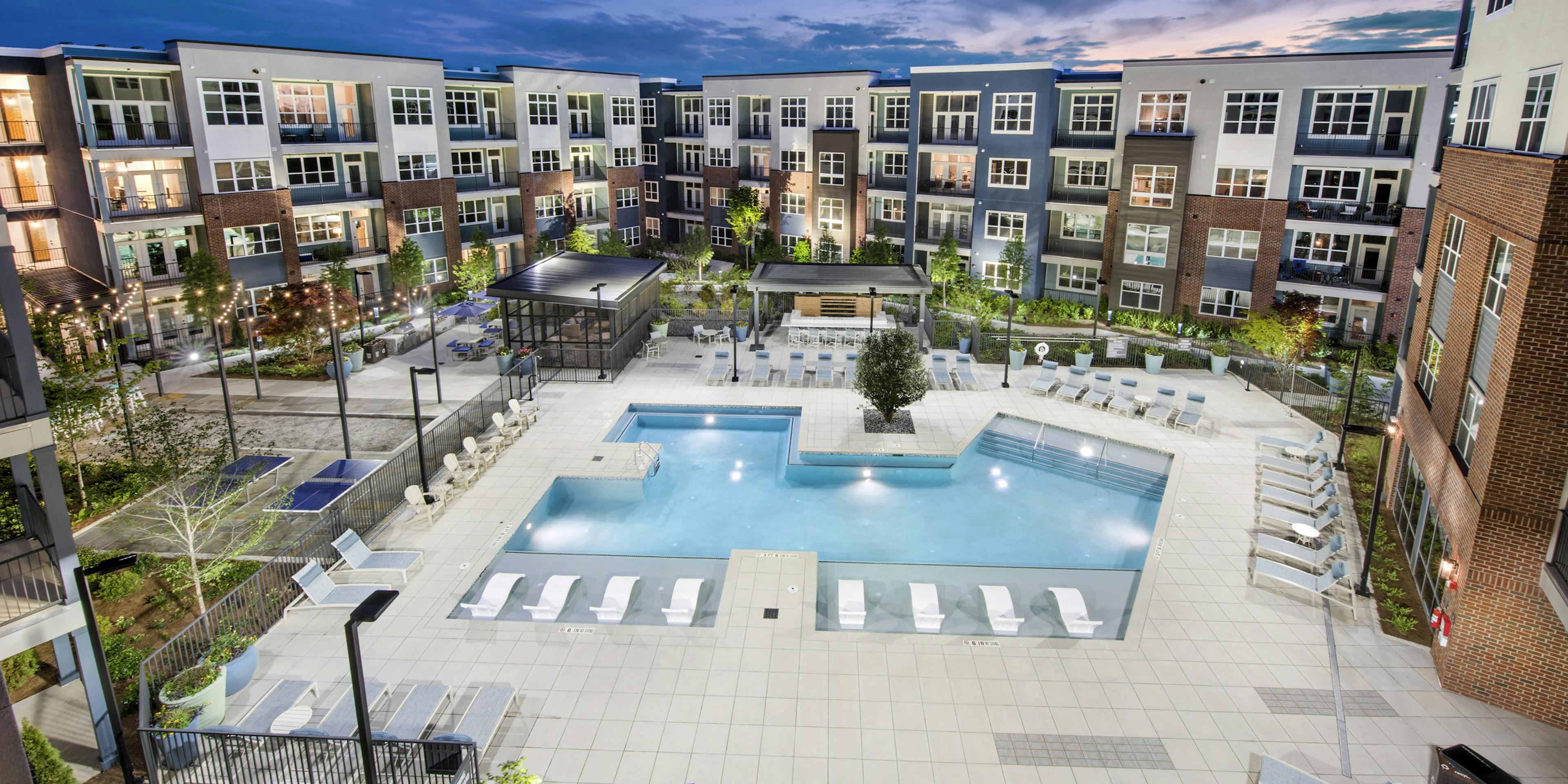 Overhead evening view of AMLI Decatur landscaped pool area with hanging lights and lounge chairs and uplit colorful building