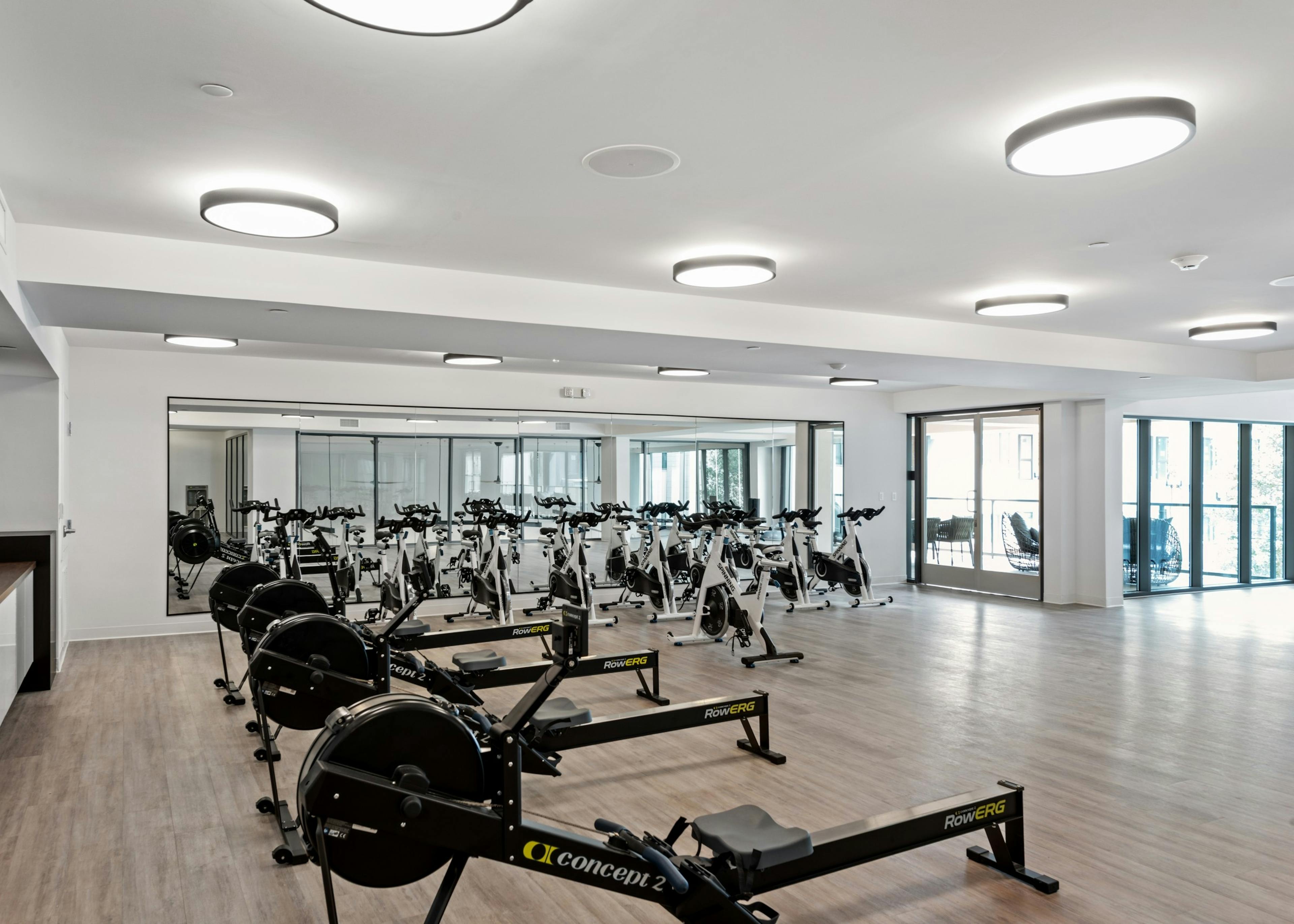 Upper level of fitness center at AMLI Old Pasadena apartments with spin bikes and row machines and big screen TV facing pool
