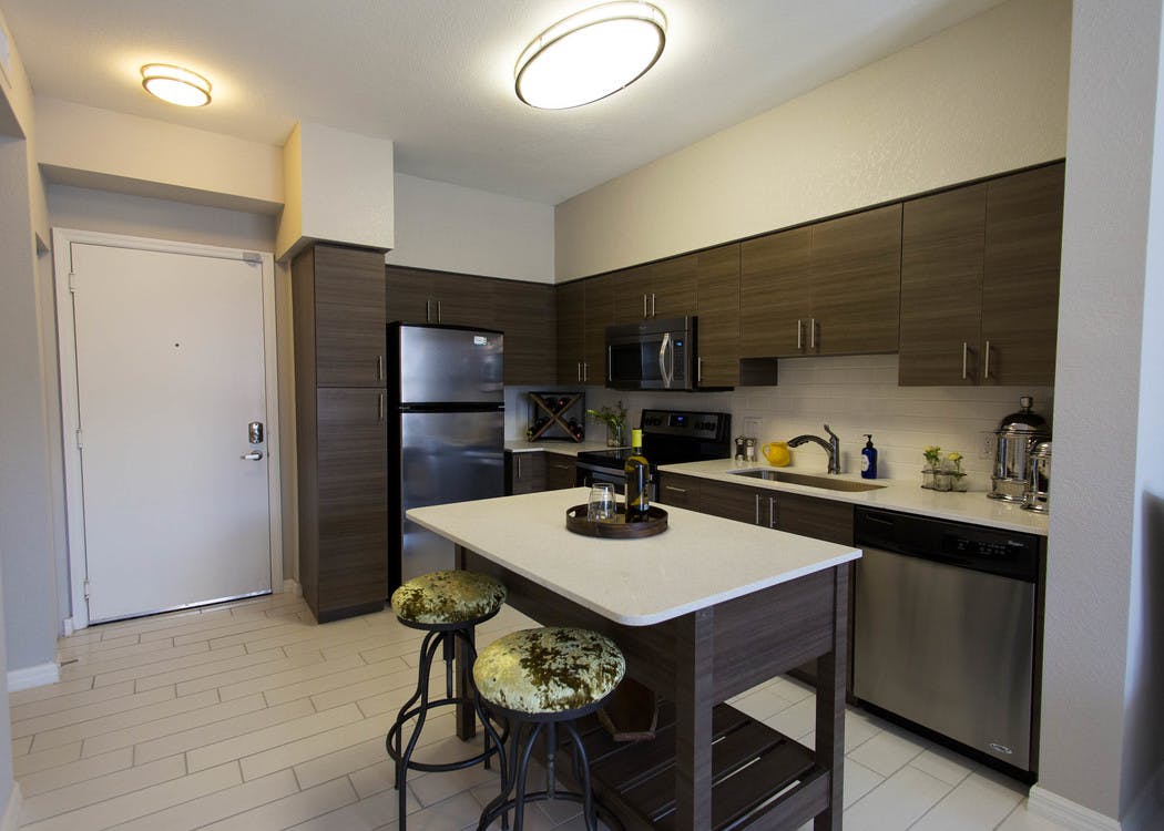 Interior view of AMLI Dadeland apartment island kitchen with stainless steel appliances and dark wood cabinetry