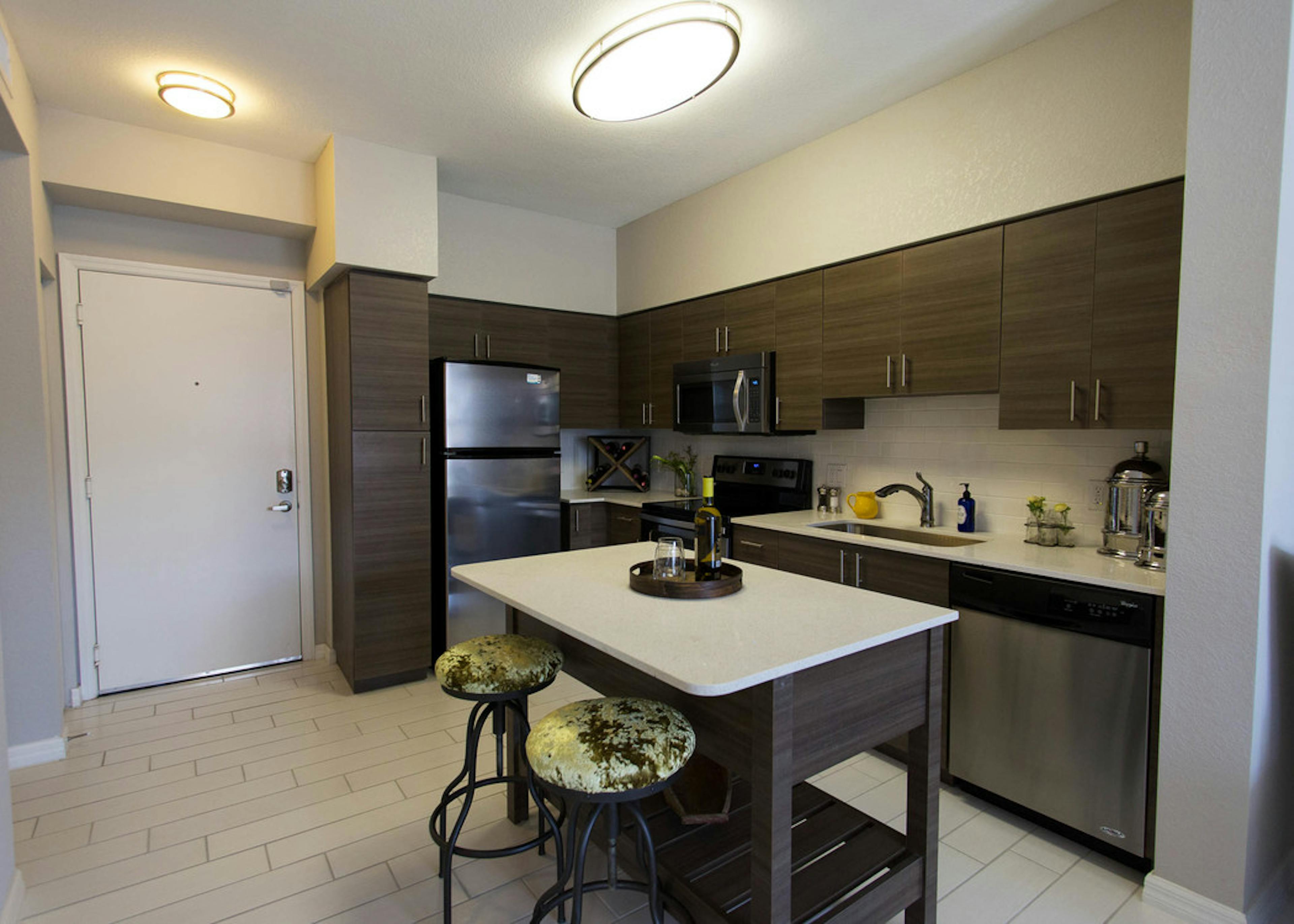  Interior view of AMLI Dadeland apartment island kitchen with stainless steel appliances and dark wood cabinetry