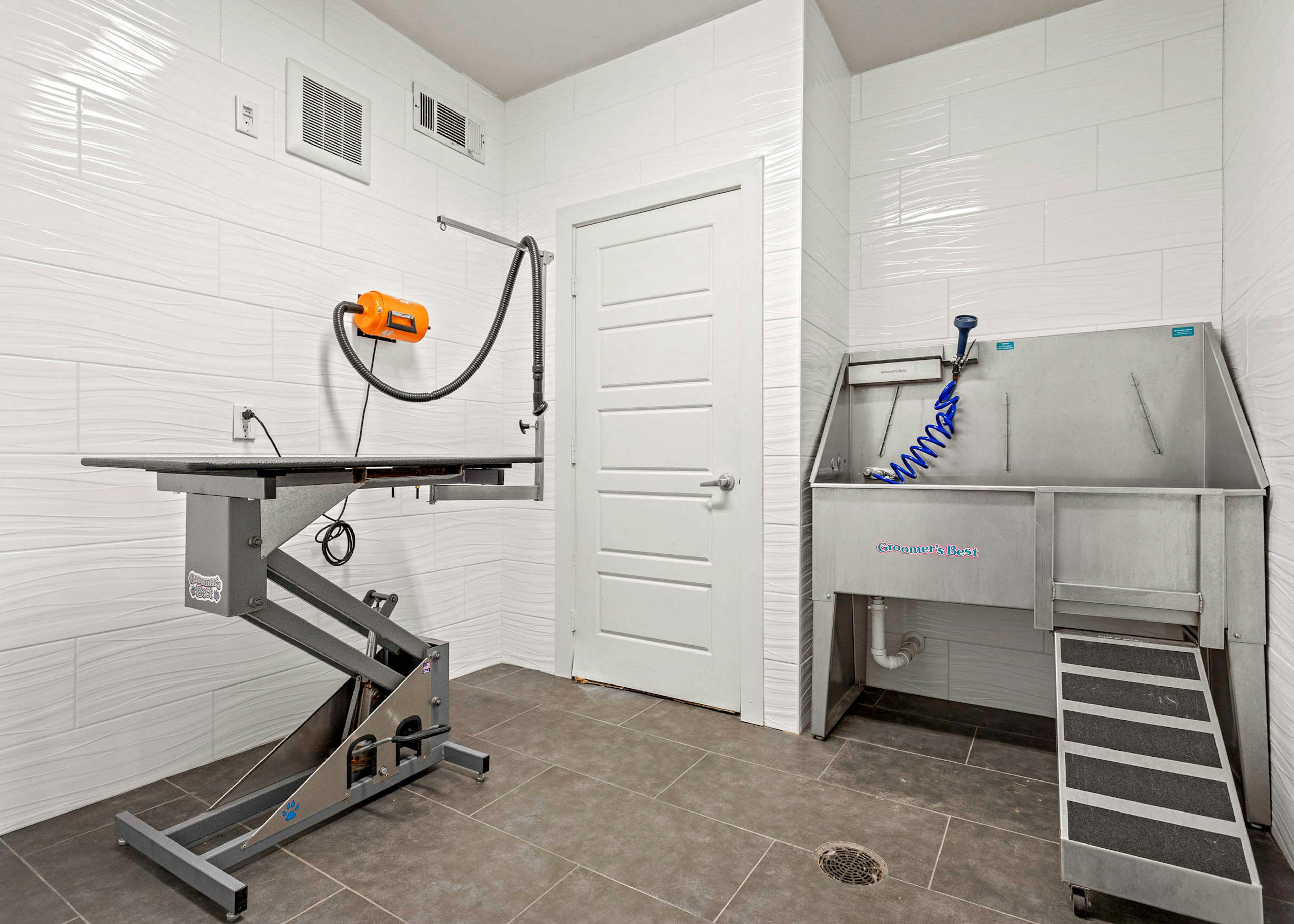 Indoor paw wash at AMLI at Escena apartments equipped with metal sink and drying station surrounded by white tiled walls