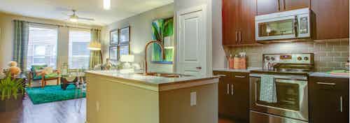 A kitchen at AMLI Riverfront Park with an island with sink and view of the oven and microwave and a look at the living room