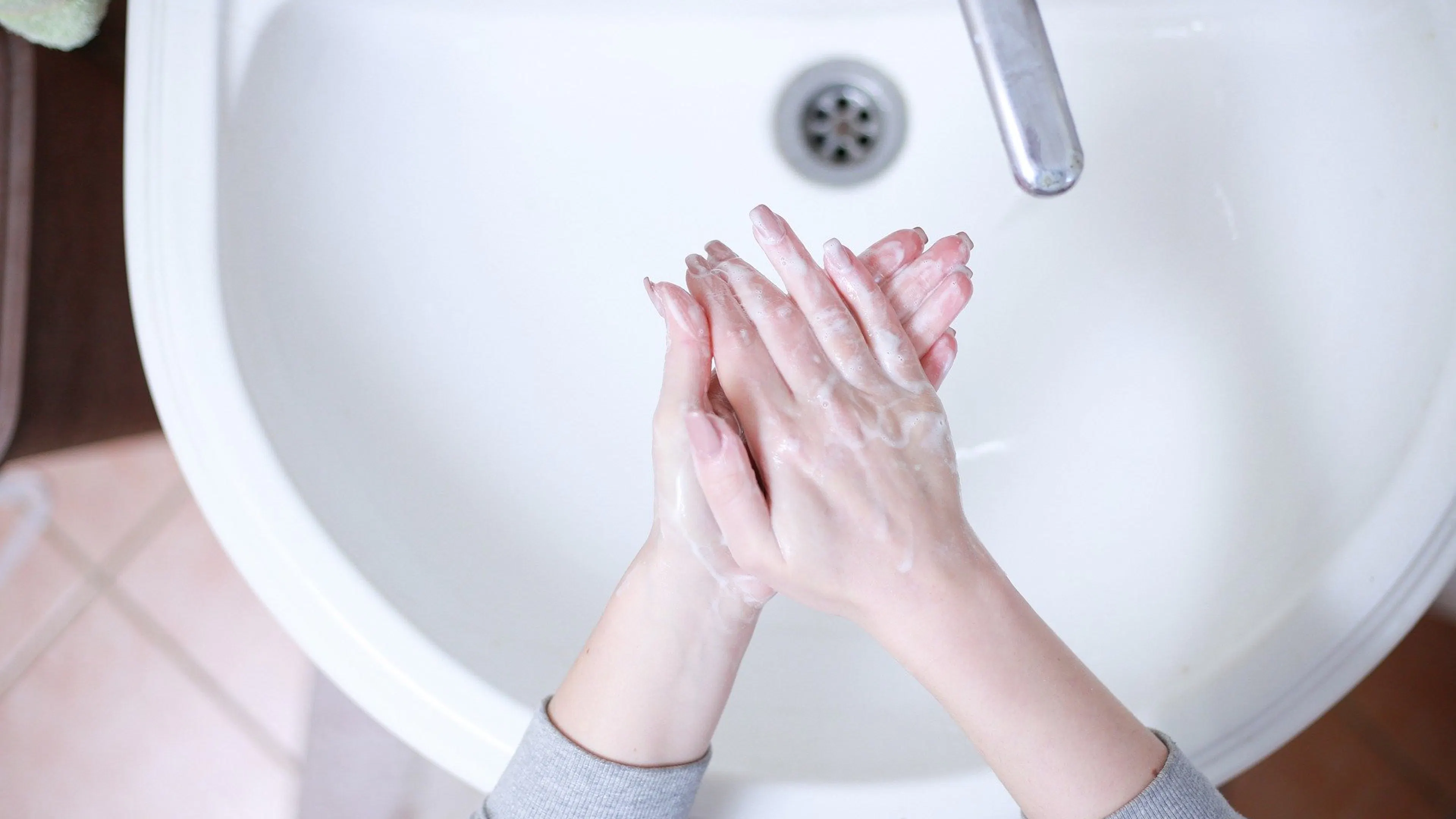 A pair of hands covered in foaming hand soap over a large porcelain sink