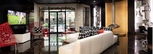 Resident lounge at AMLI Uptown apartments with white leather couch, red chairs and large TV and glass doors to pool area