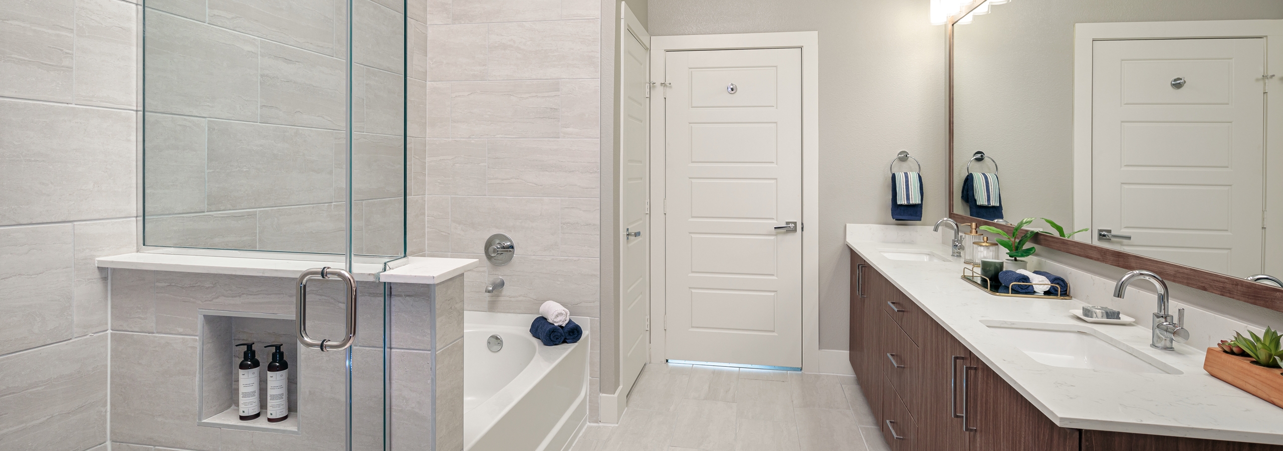 Interior of AMLI Addison bathroom with a double vanity sink and a garden tub with frameless glass shower with grey wall tiles