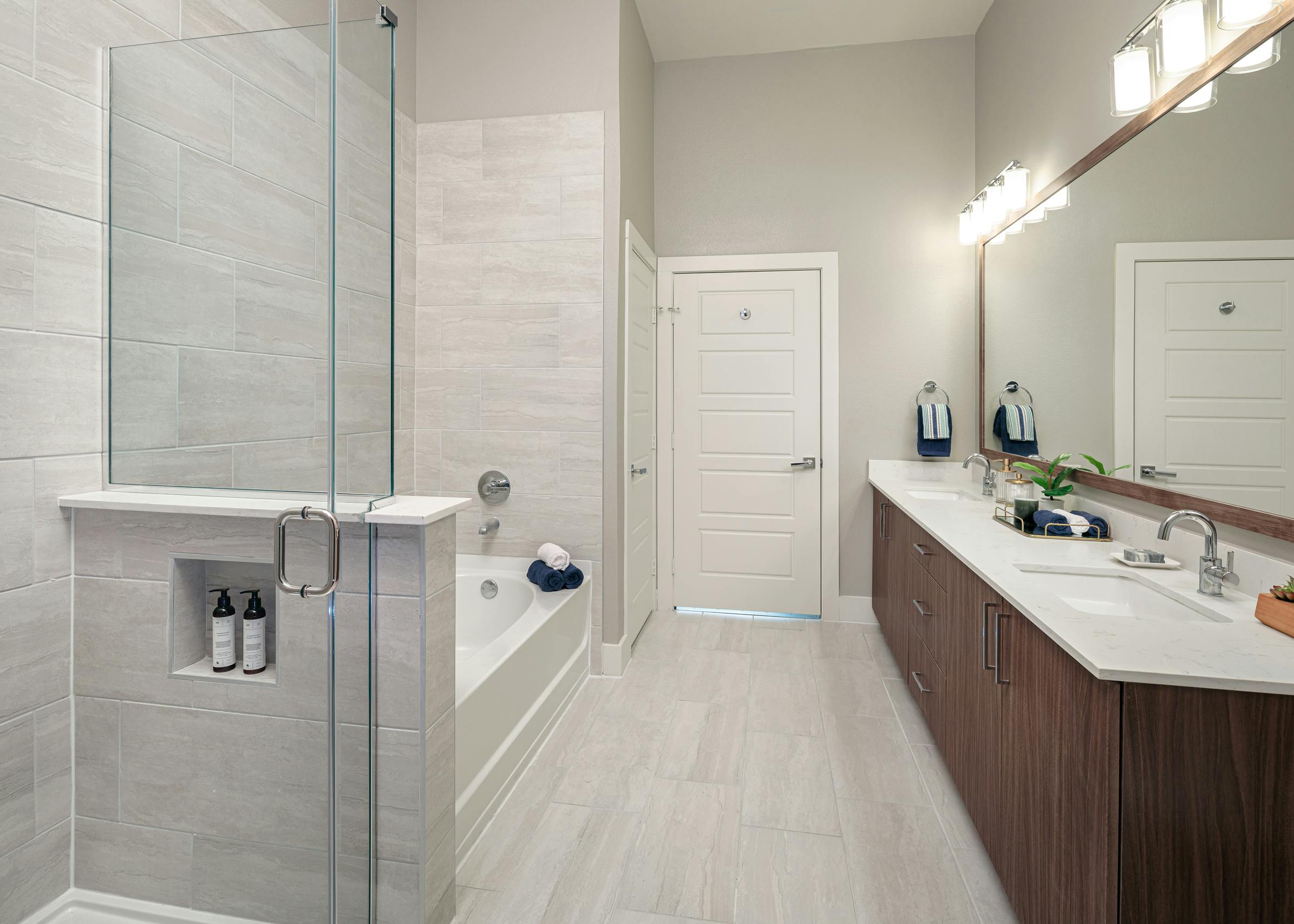 Interior of AMLI Addison bathroom with a double vanity sink and a garden tub with frameless glass shower with grey wall tiles