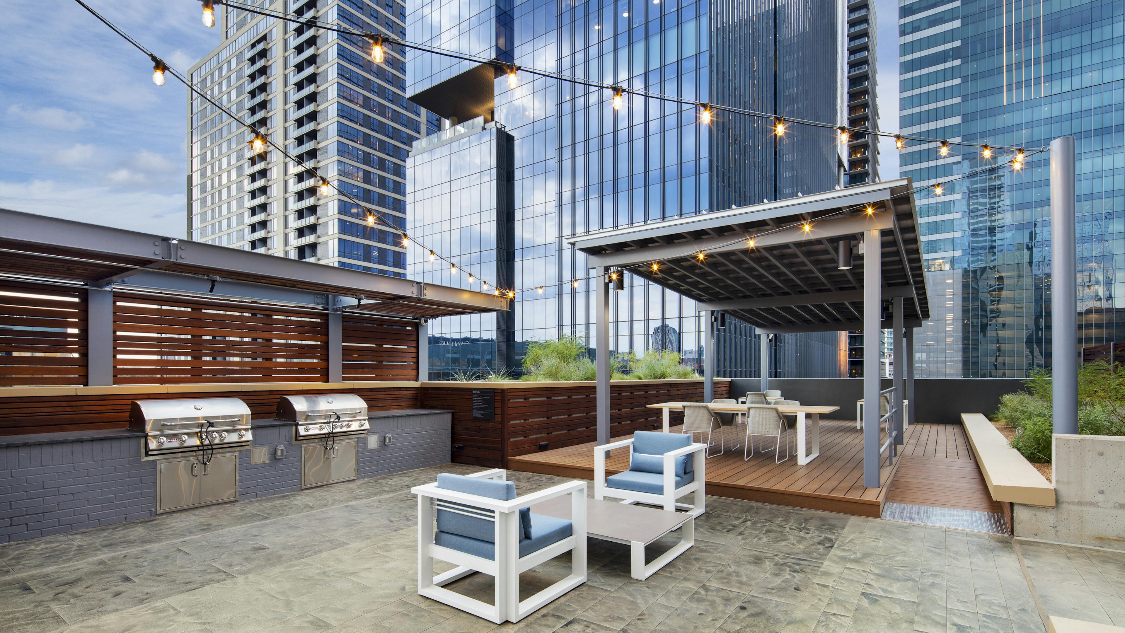 Outdoor grill area at AMLI on 2ND apartment building with two steel grills and a dining area shaded by a gray metal cabana