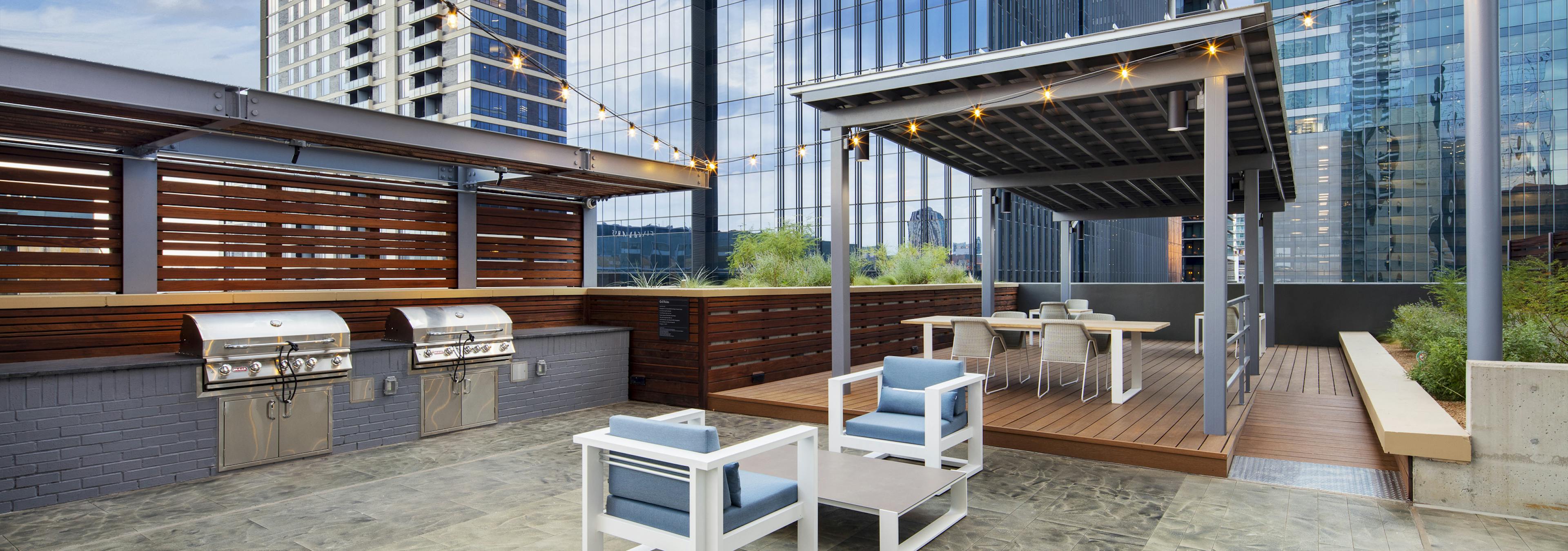 Outdoor grill area at AMLI on 2ND apartment building with two steel grills and a dining area shaded by a gray metal cabana