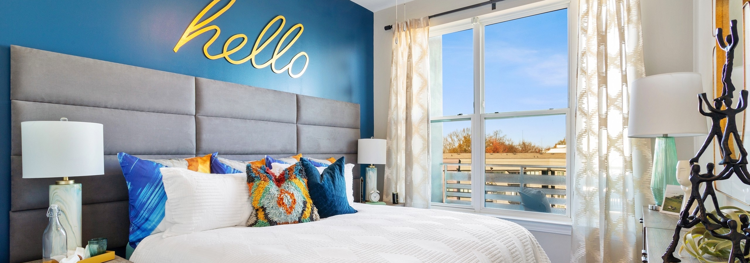 View of master bedroom at AMLI Westside apartments with king bed and blue wall with big yellow letters spelling out hello
