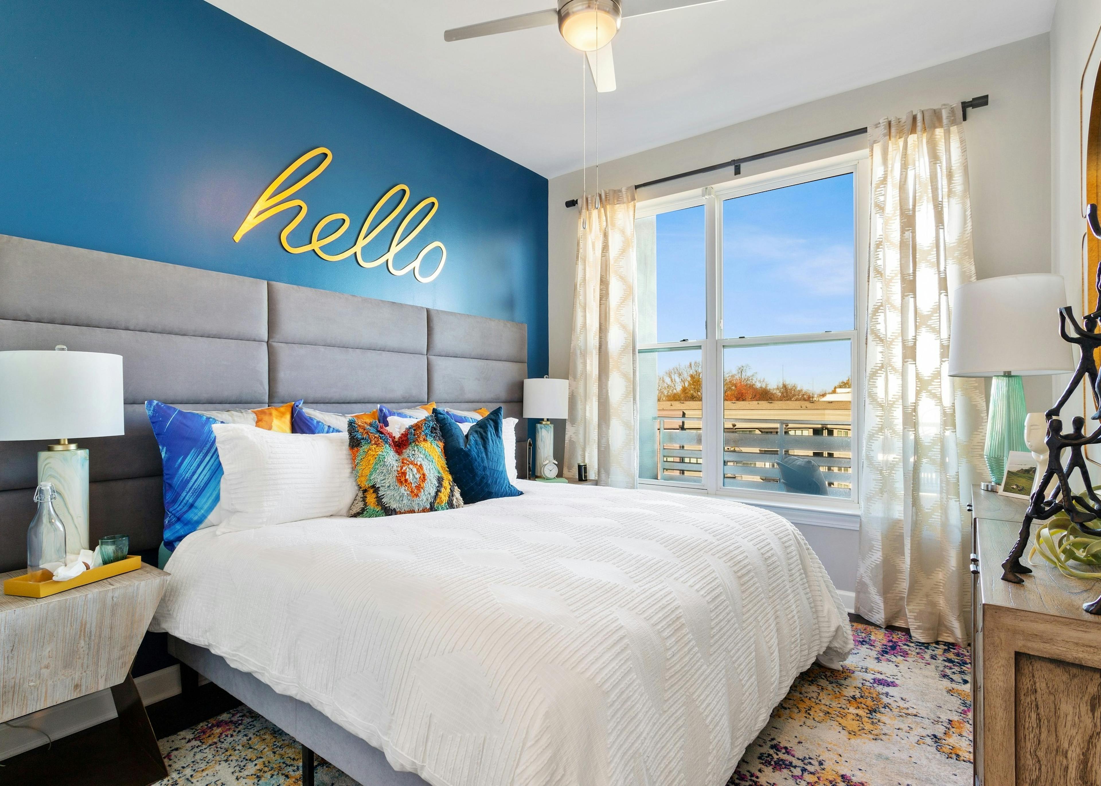 View of master bedroom at AMLI Westside apartments with king bed and blue wall with big yellow letters spelling out hello