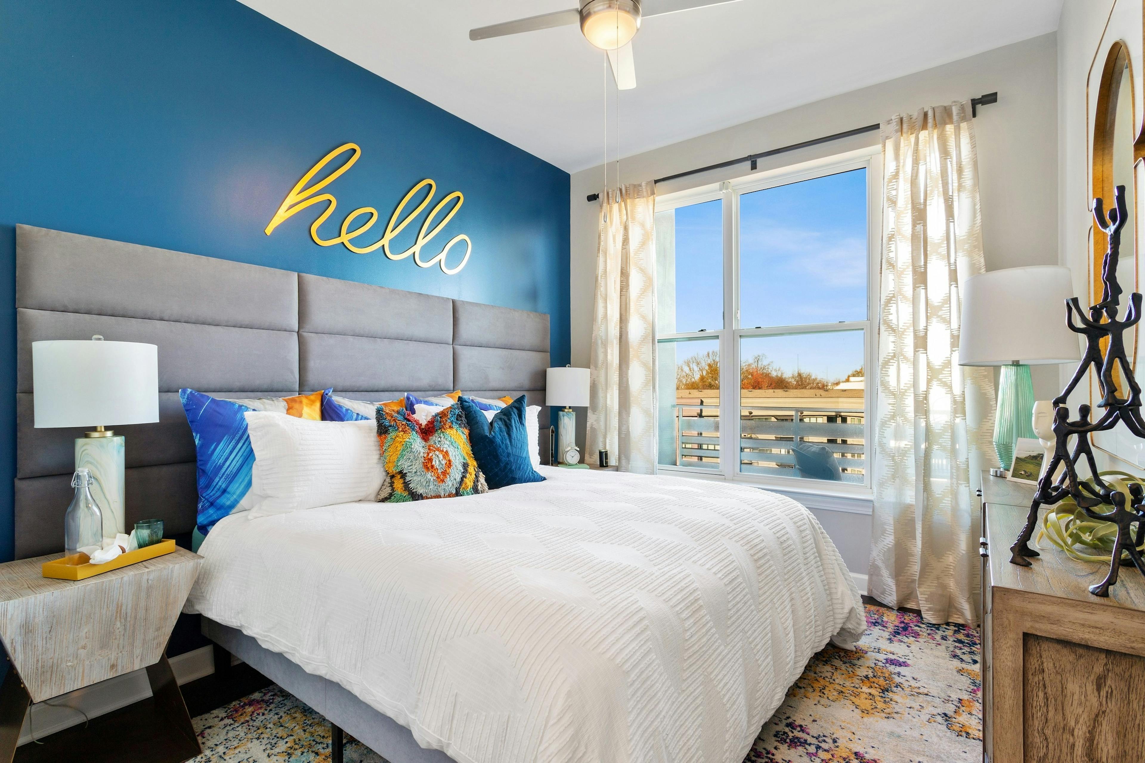 View of master bedroom at AMLI Westside apartments with king bed and blue wall with big yellow letters spelling out hello