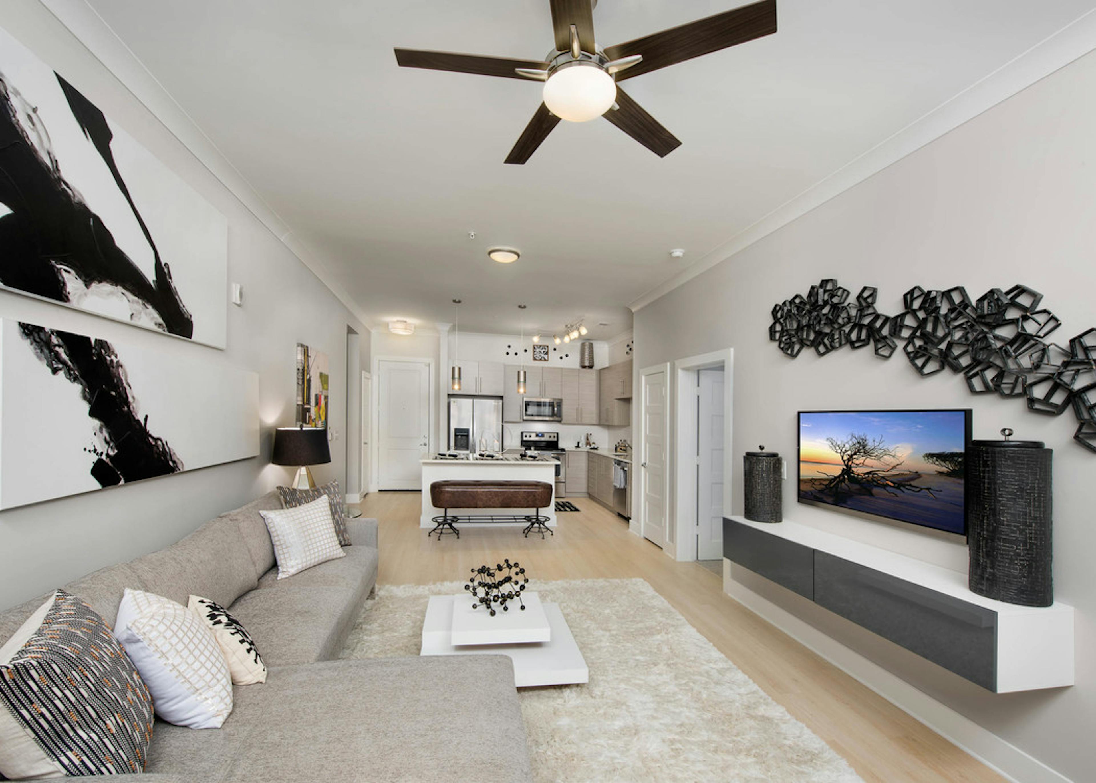 Living room at AMLI Buckhead with a beige couch and black and white wall decor with light wood floors leading to kitchen area