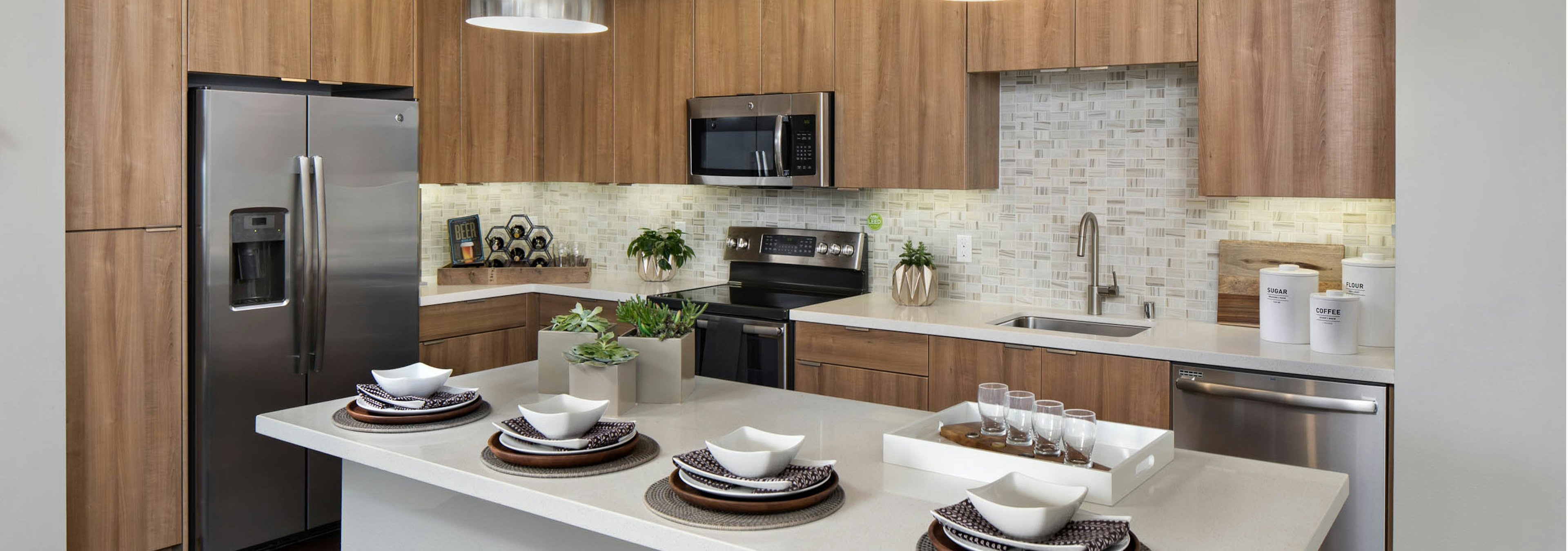 AMLI Uptown Orange apartment kitchen with light wood cabinets and designer tile backsplash and stainless steel appliances