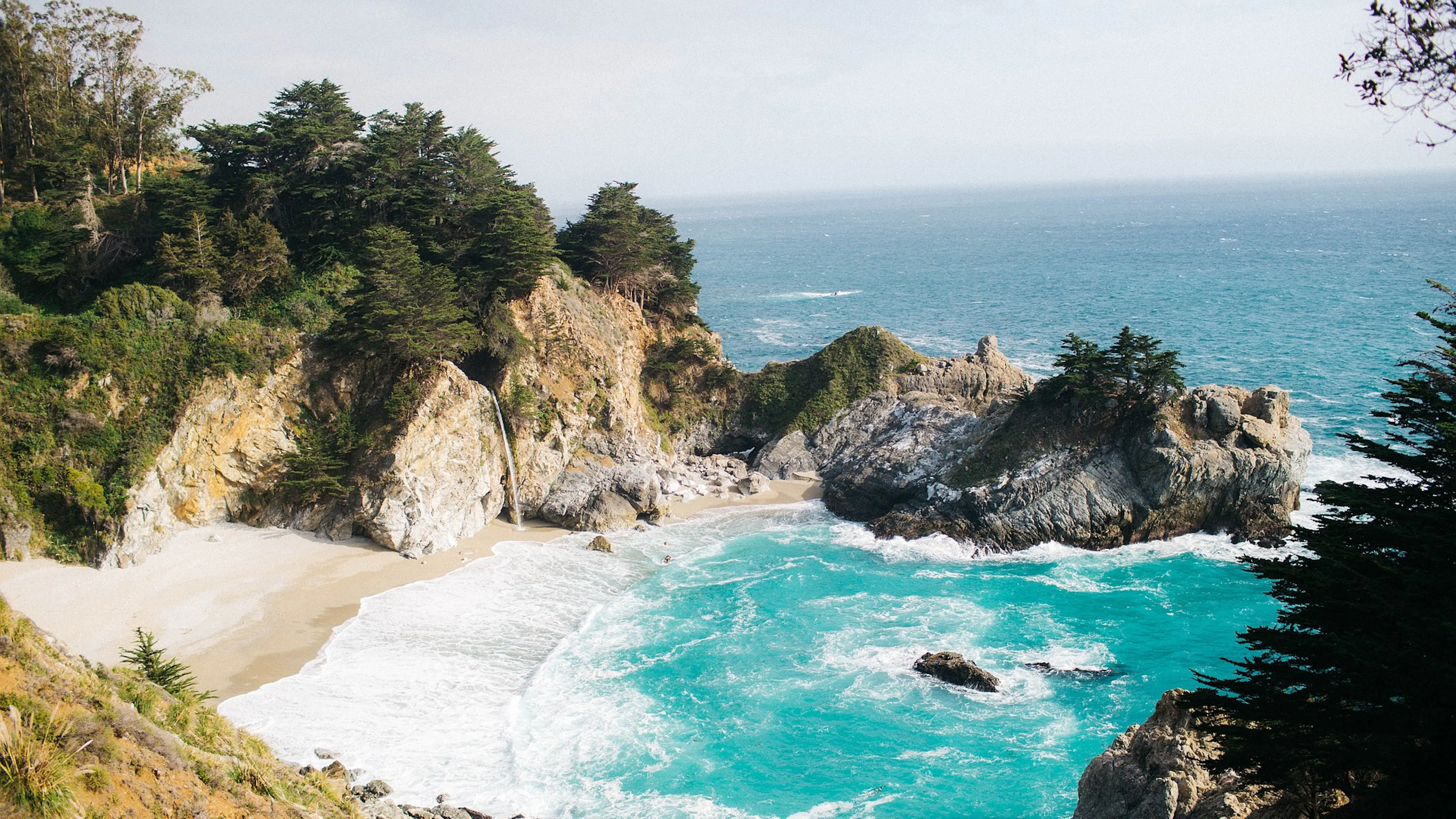 An ocean cove surrounded by rock formations and trees and crystal blue water