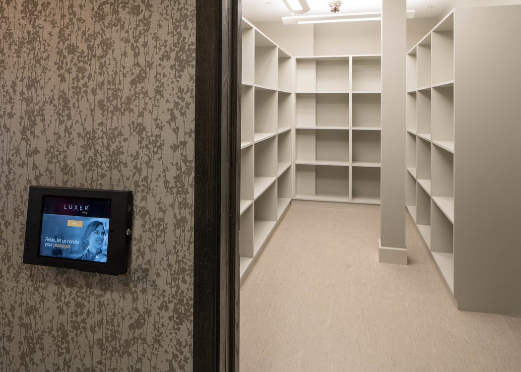 Interior of luxer package amenity at AMLI Deerfield with iPad on outside of doorway and wall to wall shelving inside room