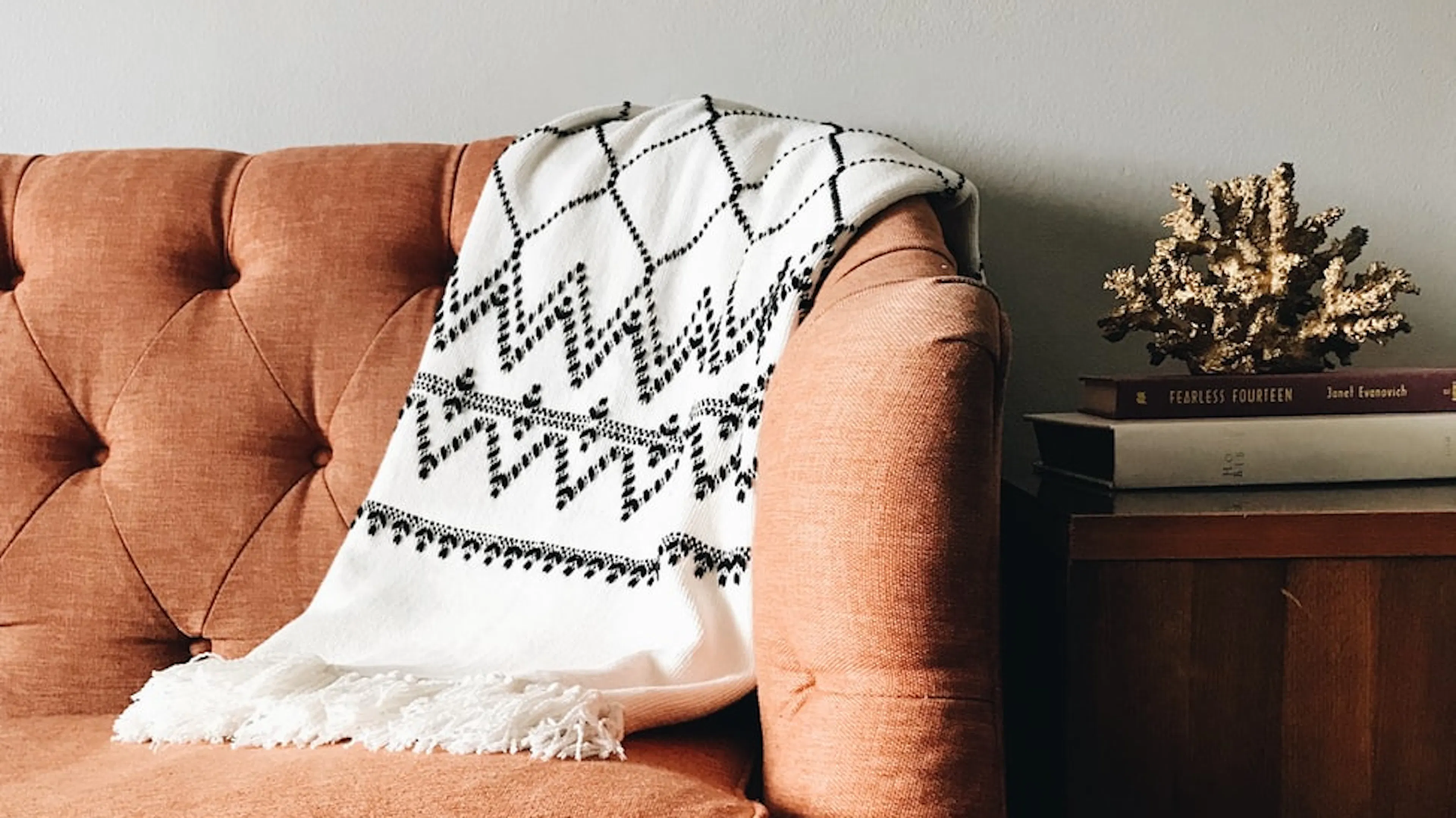 Brown couch with a white and black patterned blanket folded on the arm. 