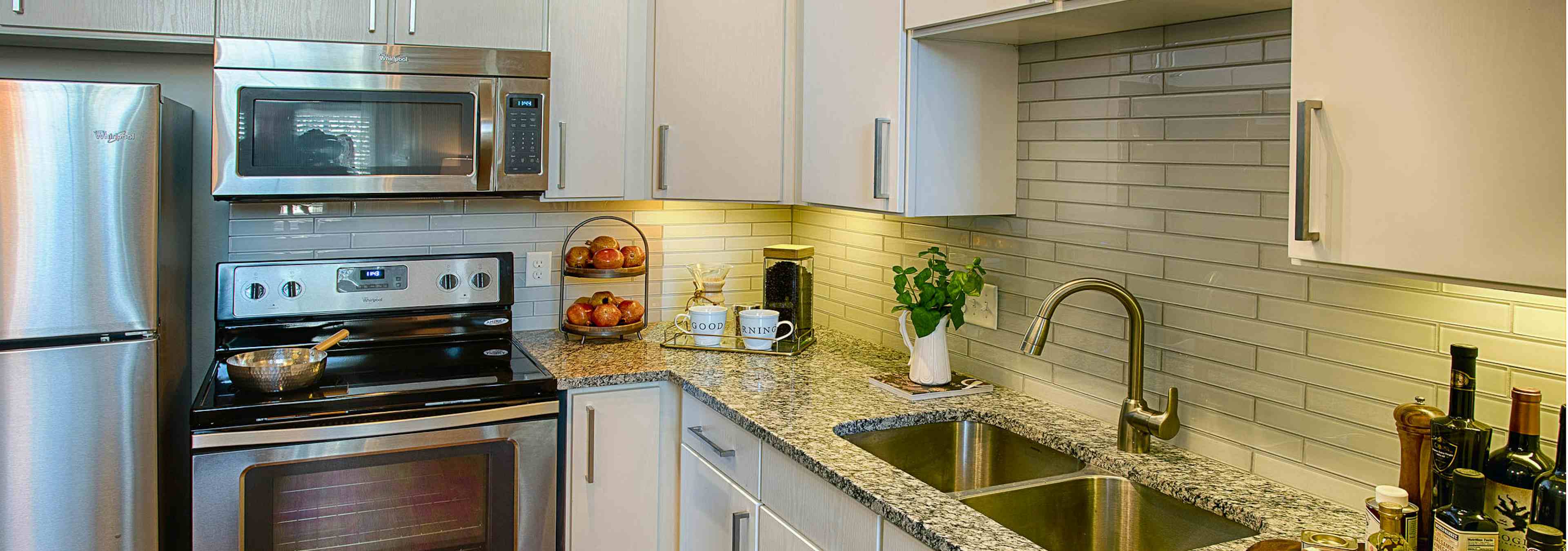 A kitchen at AMLI Denargo Market apartments with a tile back splash with white cupboards and an oven with overhead microwave