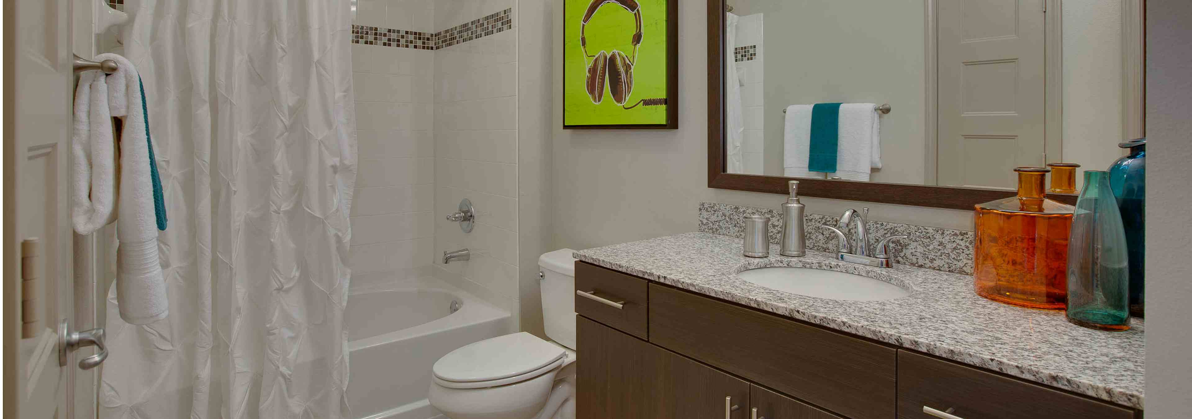 Interior view of AMLI Ponce Park bathroom with a single dark wood vanity with a toilet and white tiled shower tub