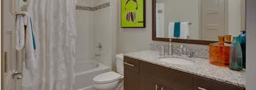 Interior view of AMLI Ponce Park bathroom with a single dark wood vanity with a toilet and white tiled shower tub