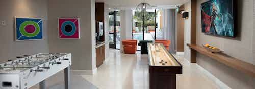 Interior game lounge at AMLI 8800 with shuffleboard table, foosball, coffee bar, TV and colorful artwork on the walls
