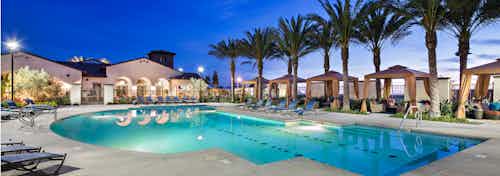 Nighttime close-up view of AMLI Spanish Hills apartment swimming pool area with lounge seating, five cabanas and palm trees