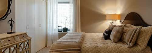 An AMLI 900 bedroom featuring neutral decor and white closet doors by a window with daytime city views and flowing curtains