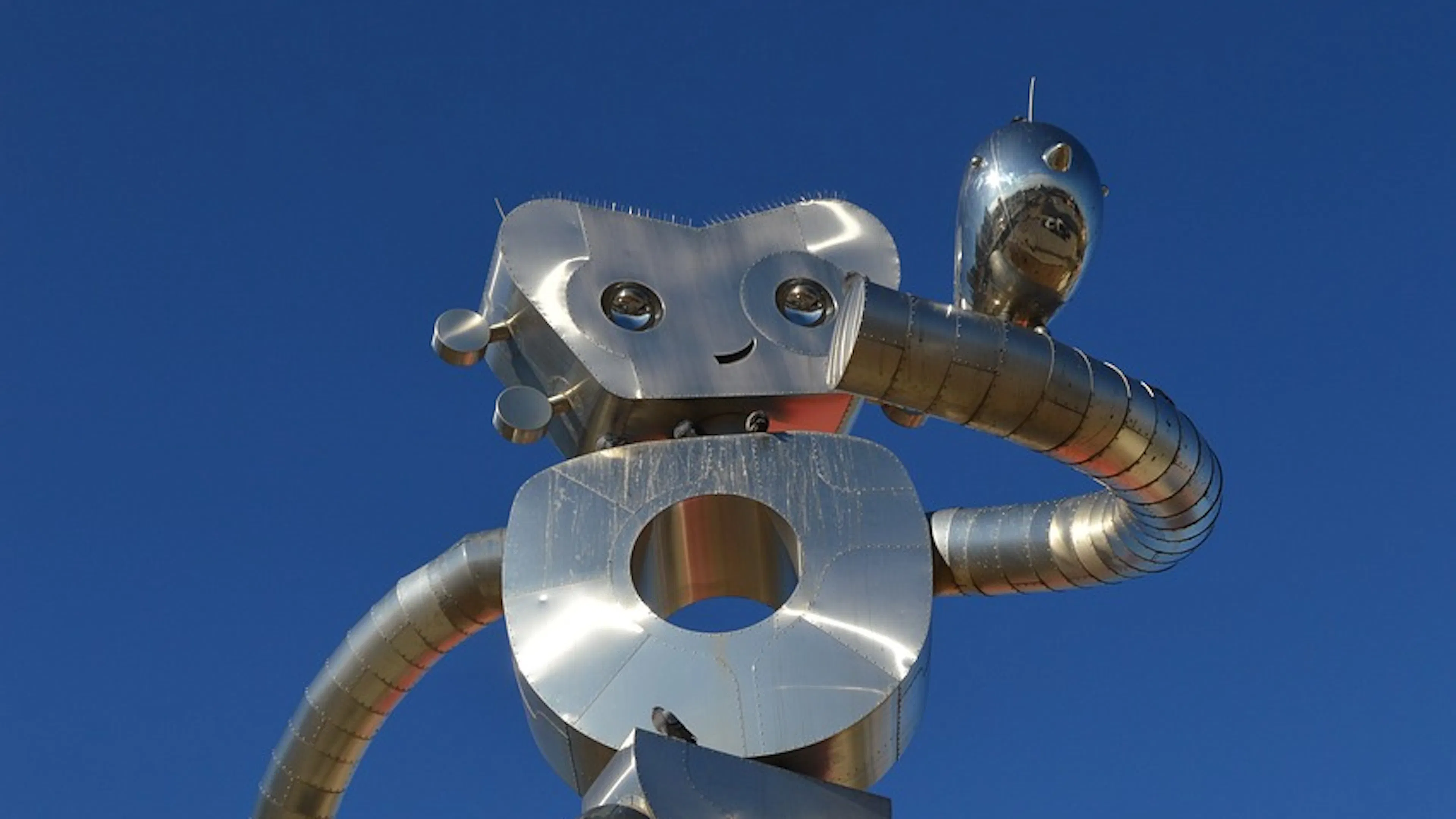 A tall statue of the Dallas Traveling Man with its robotic slinky looking arms outstretched to hold a smaller bird statue