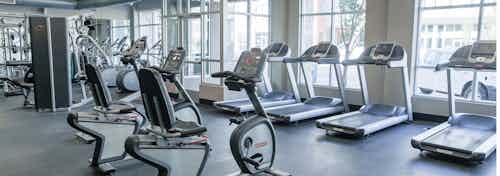 Fitness center at AMLI Arista apartments with multiple treadmills and stationary bicycles with several mirrors and windows