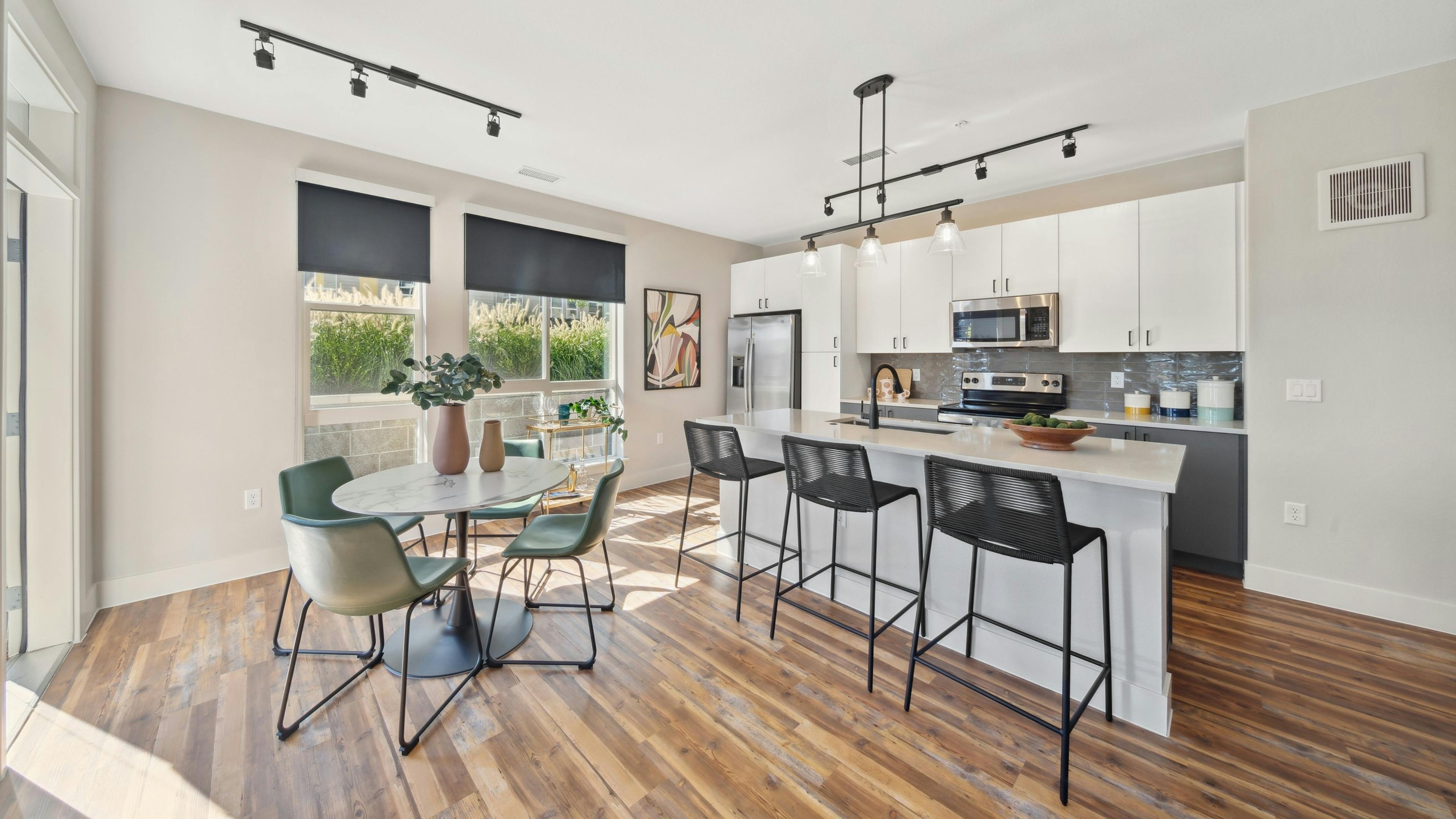 Kitchen with large white island and black bar stools and table and green chairs and white cabinets at AMLI RiNo apartments