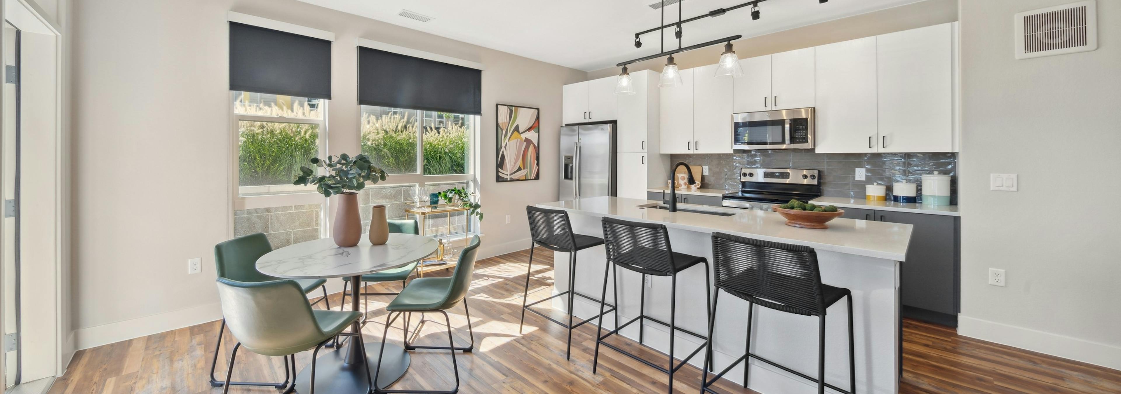 Kitchen with large white island and black bar stools and table and green chairs and white cabinets at AMLI RiNo apartments