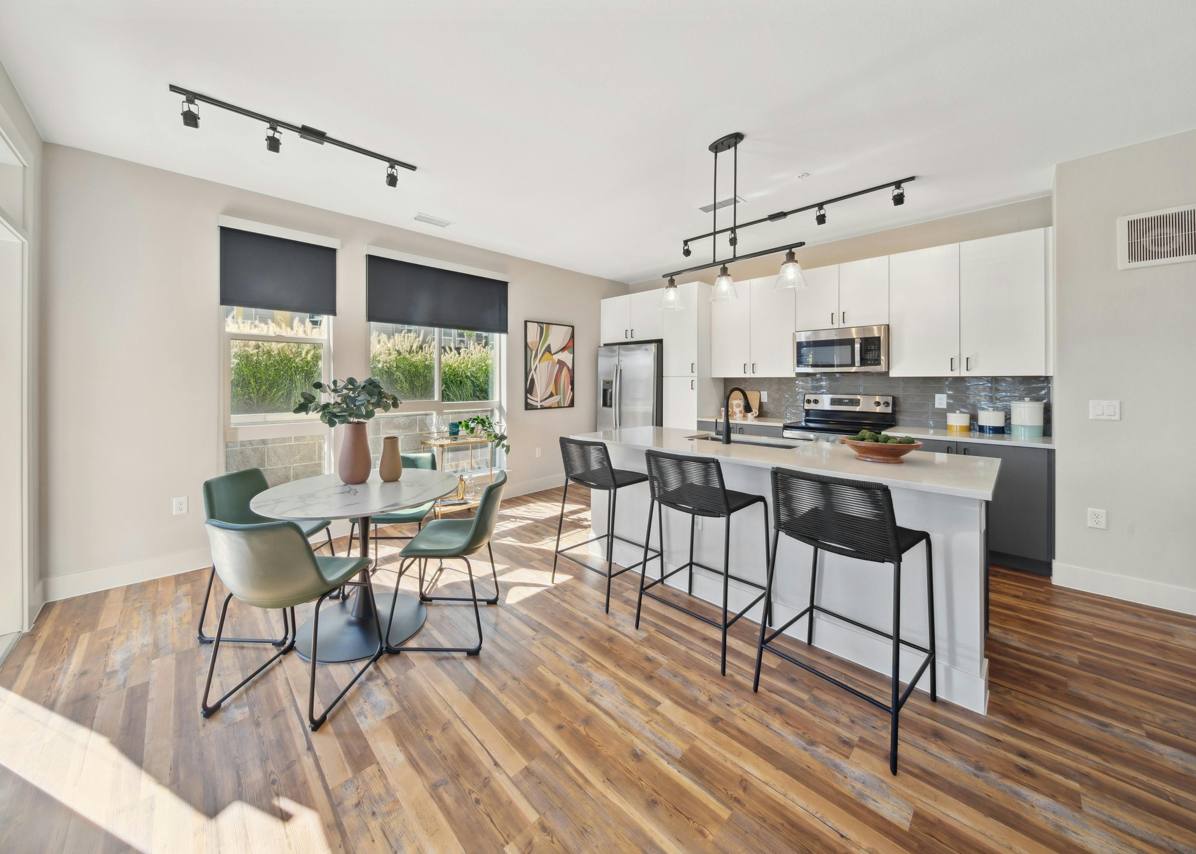 Kitchen with large white island and black bar stools and table and green chairs and white cabinets at AMLI RiNo apartments