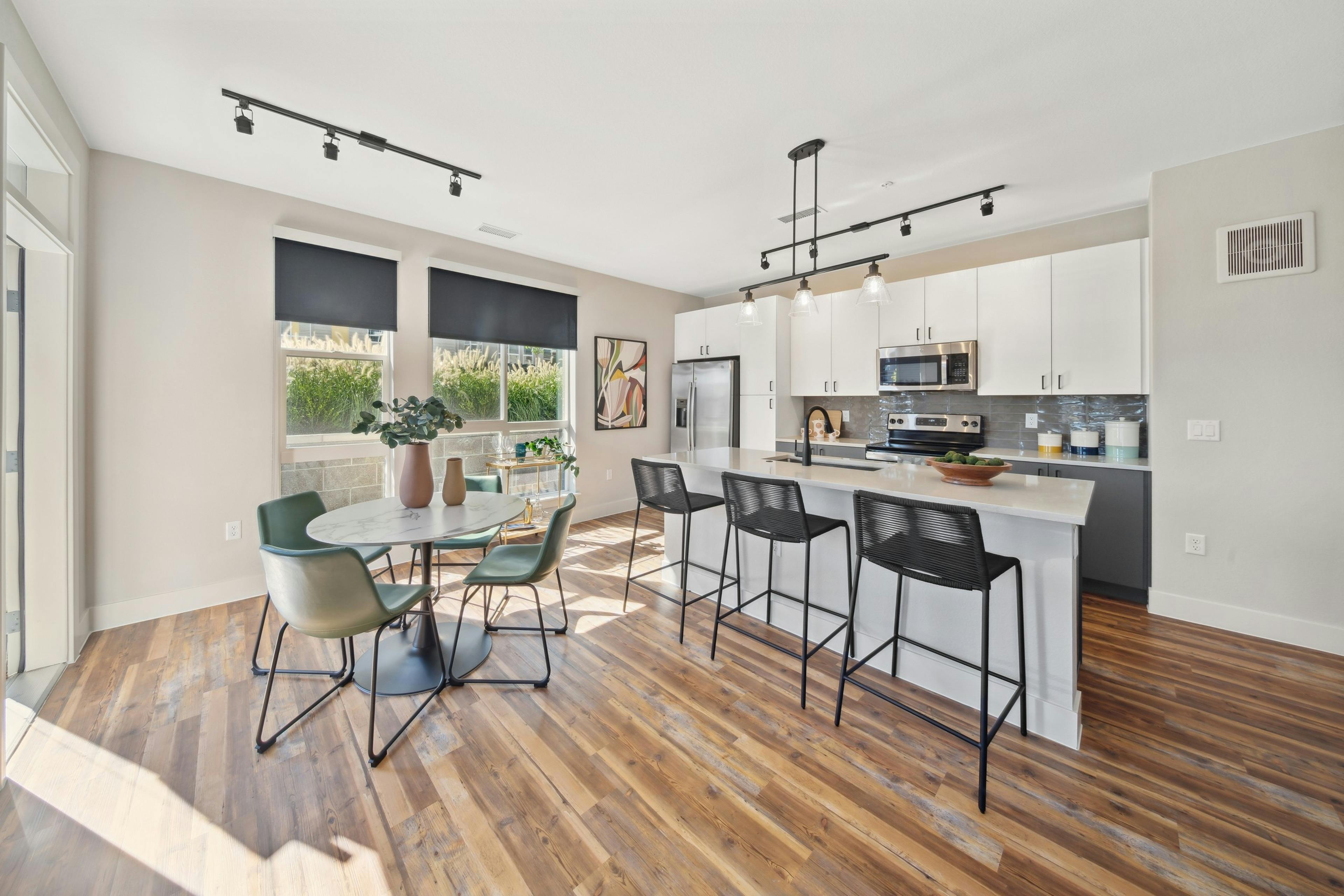 Kitchen with large white island and black bar stools and table and green chairs and white cabinets at AMLI RiNo apartments