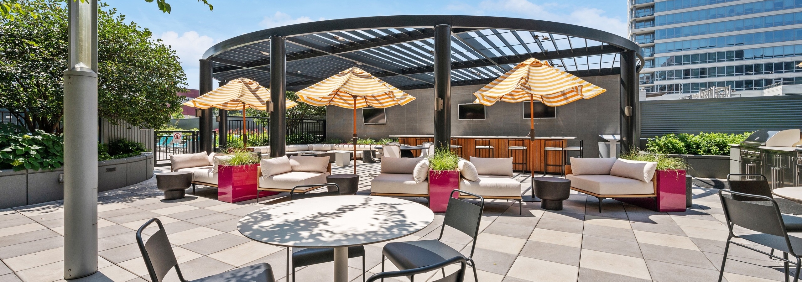 View of amenity deck lounge with dining tables and umbrella shaded patio furniture open to pergola covered bar at AMLI Lofts