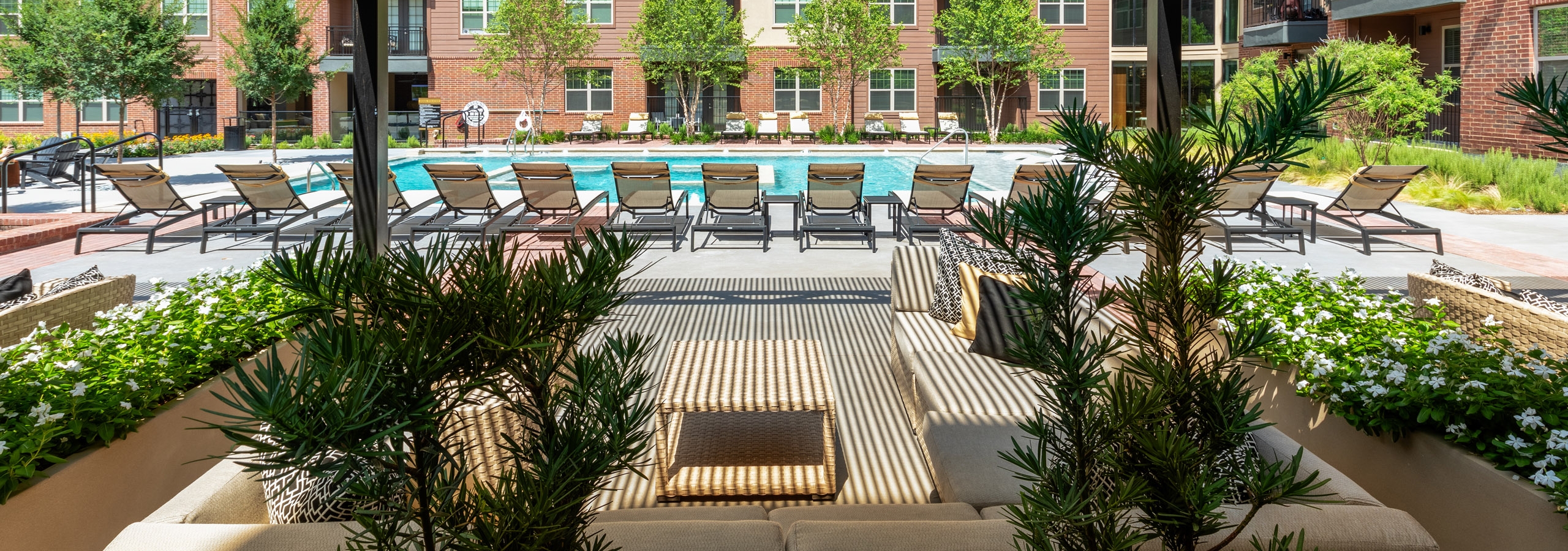 Daytime view of AMLI Grapevine apartments poolside cabana surrounded by lush greenery with a view of the pool and seating