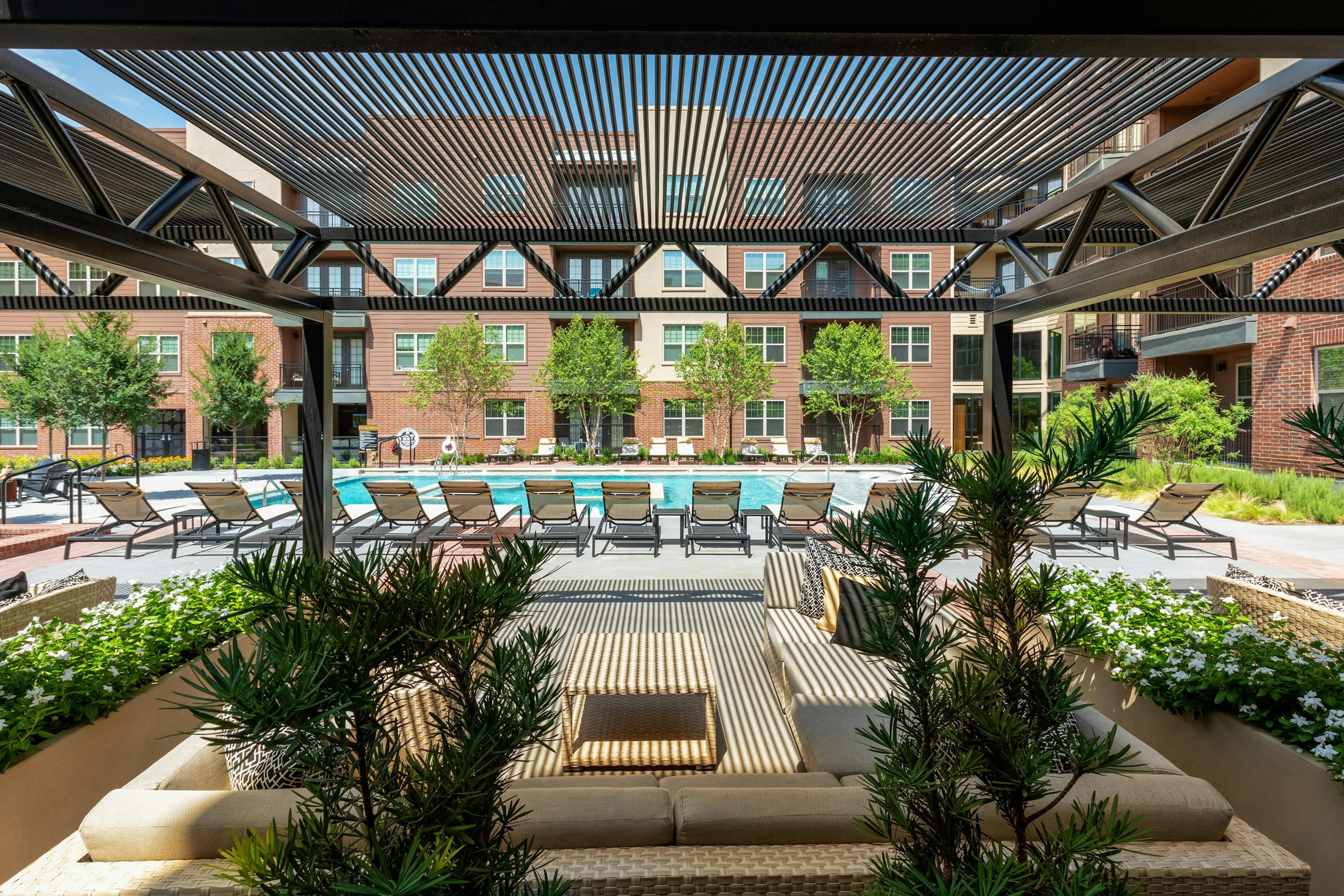 Daytime view of AMLI Grapevine apartments poolside cabana surrounded by lush greenery with a view of the pool and seating 